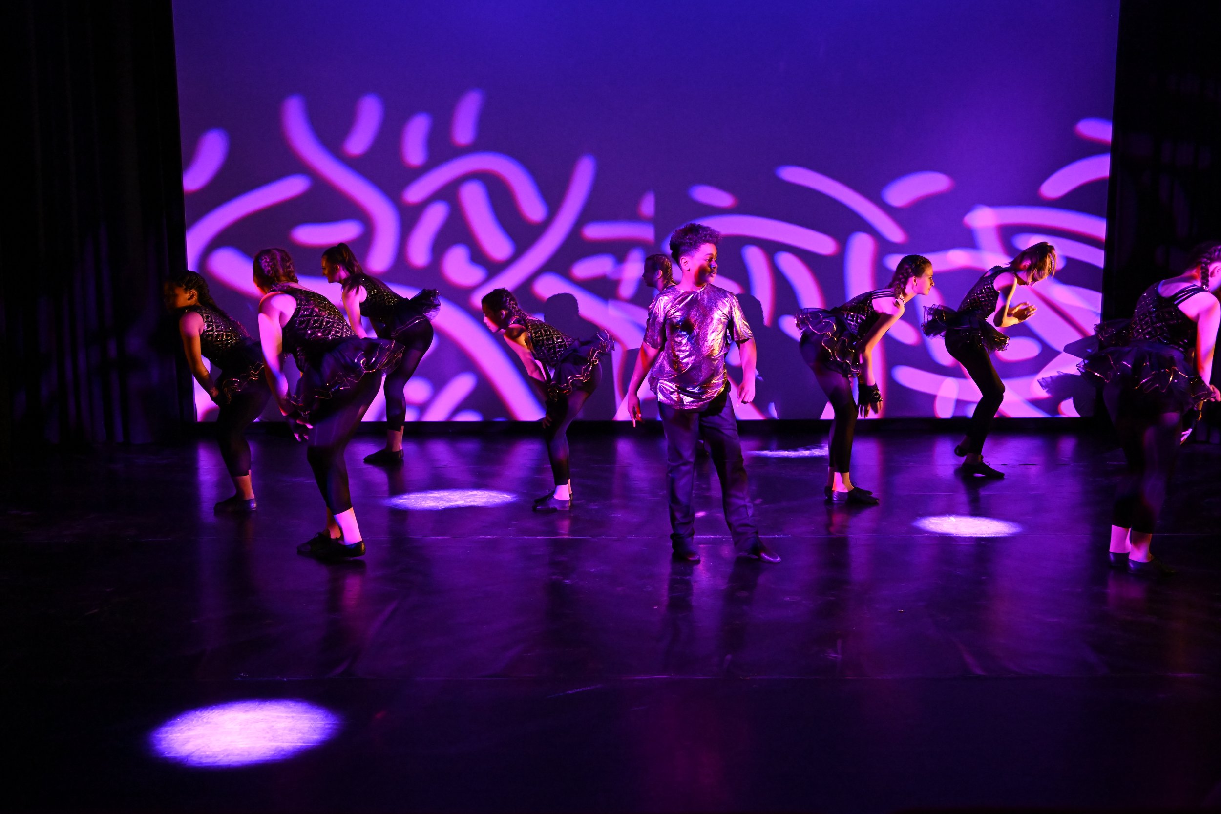 Children perform a dance on stage under purple lighting with a projected abstract background.