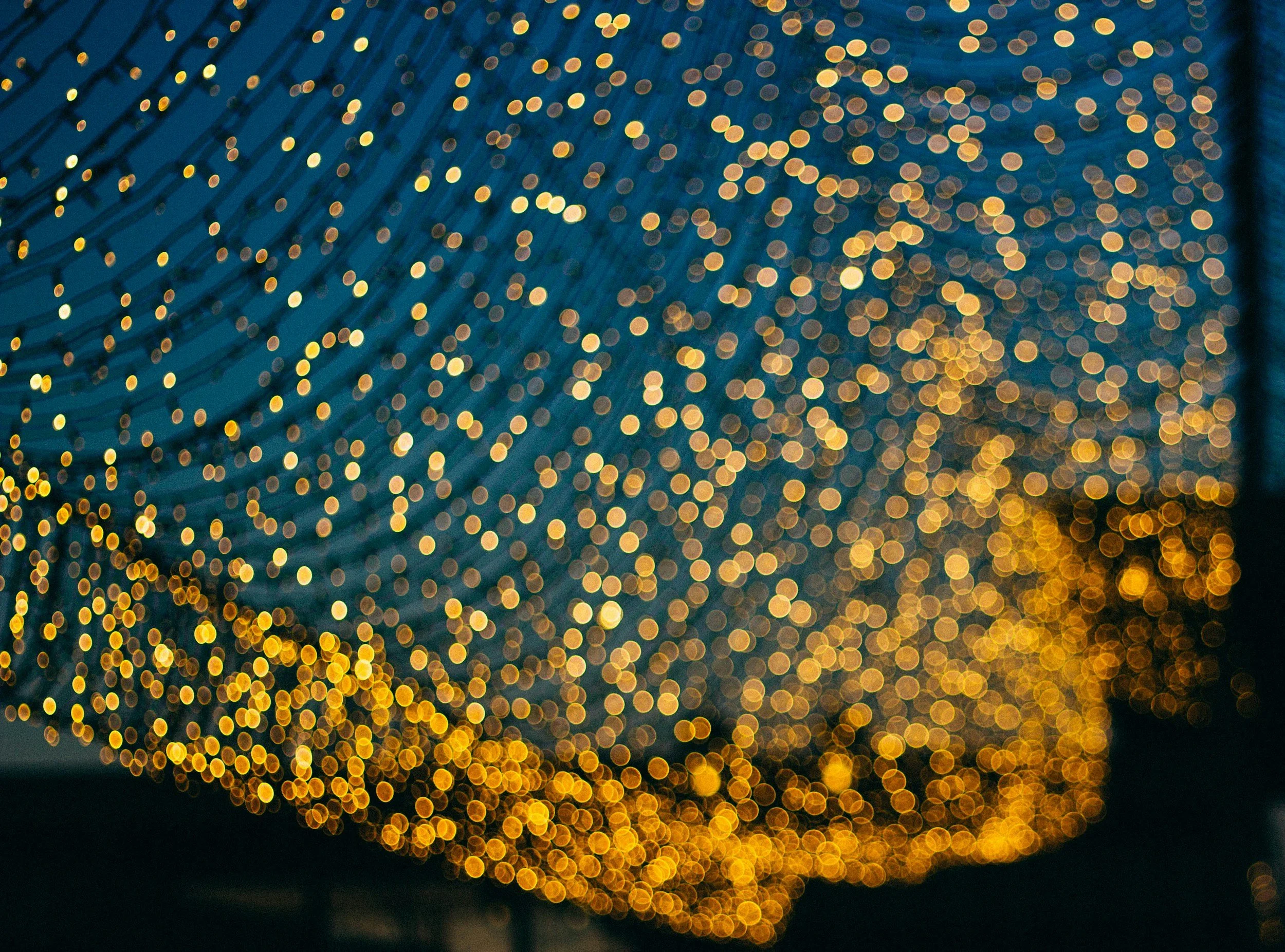 Blurred image of a chandelier with many golden lights, creating a bokeh effect.