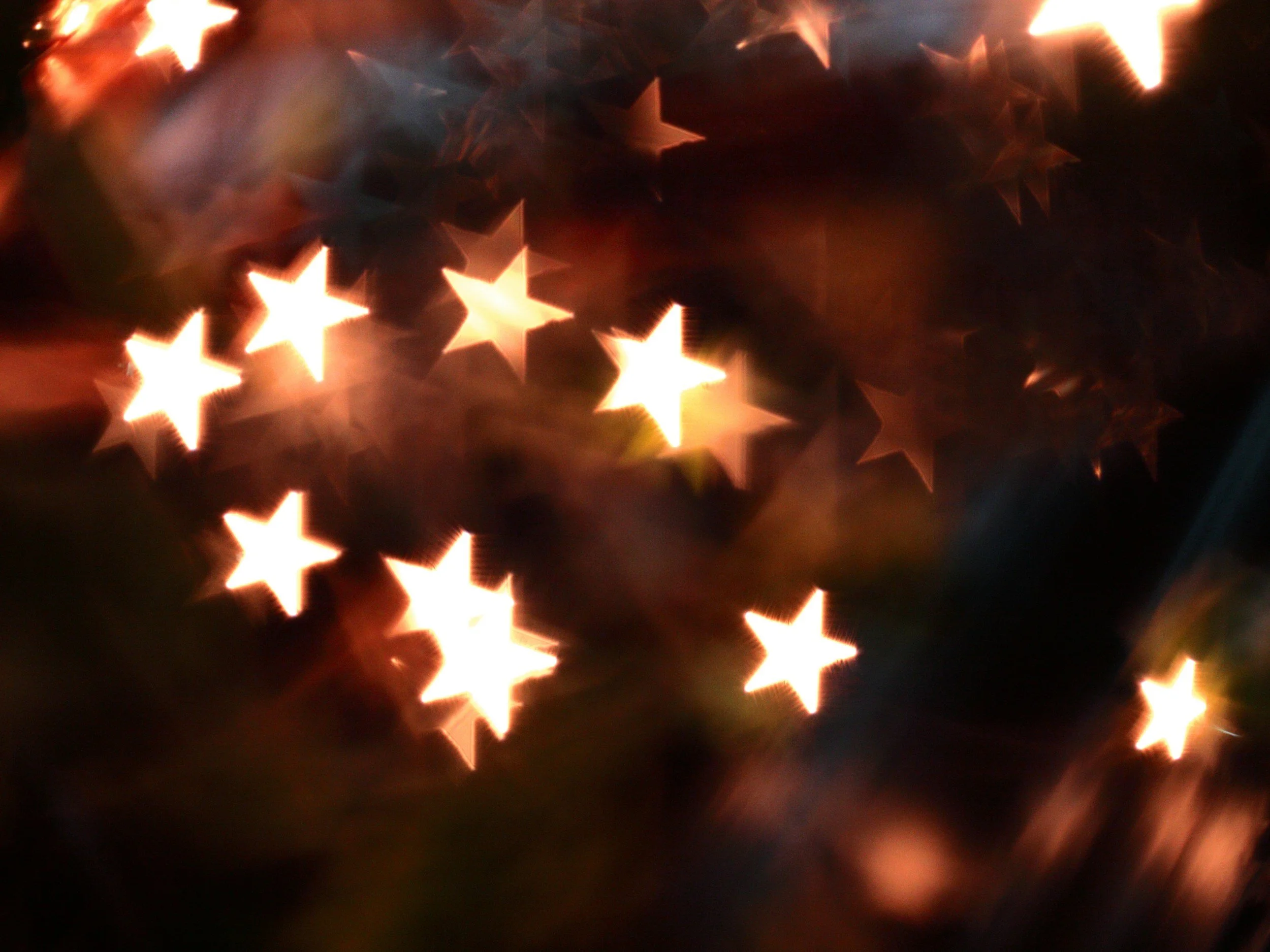 Blurred image of glowing star-shaped lights in warm tones, creating an abstract bokeh effect.