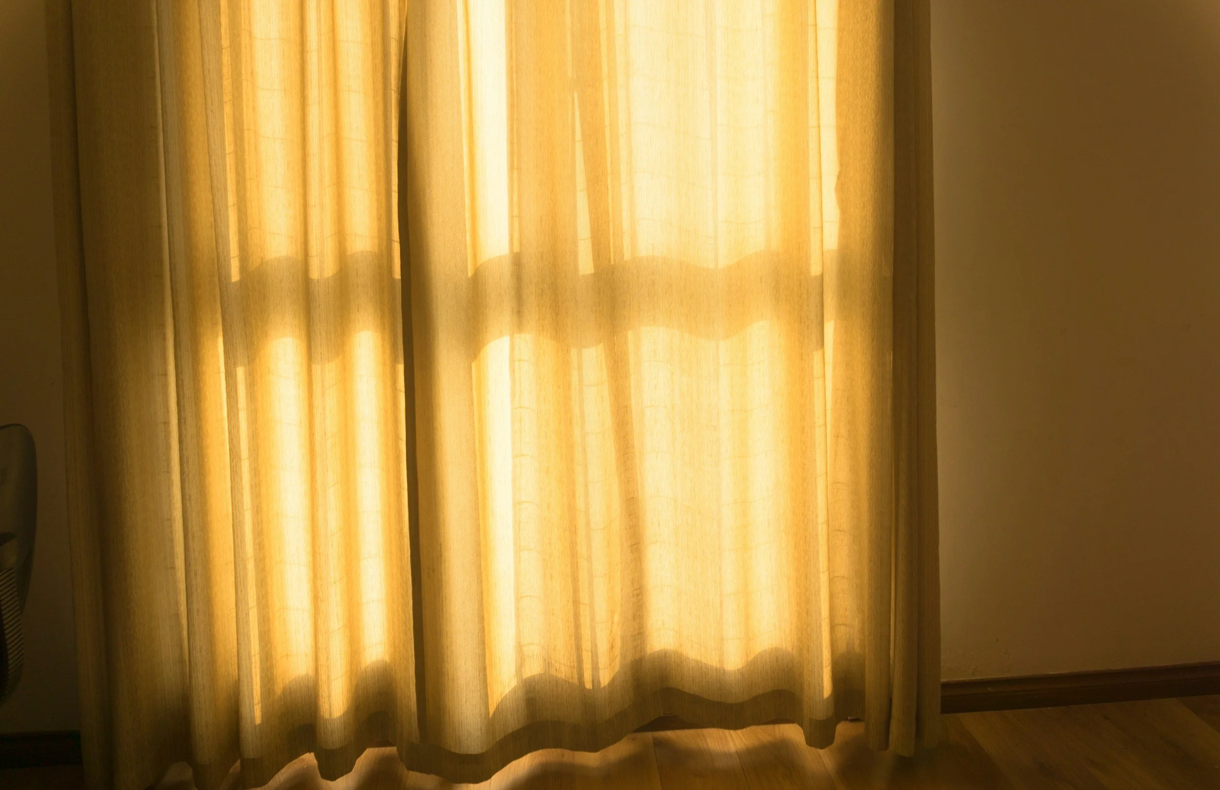 Sunlight shining through beige curtains onto a wooden floor.