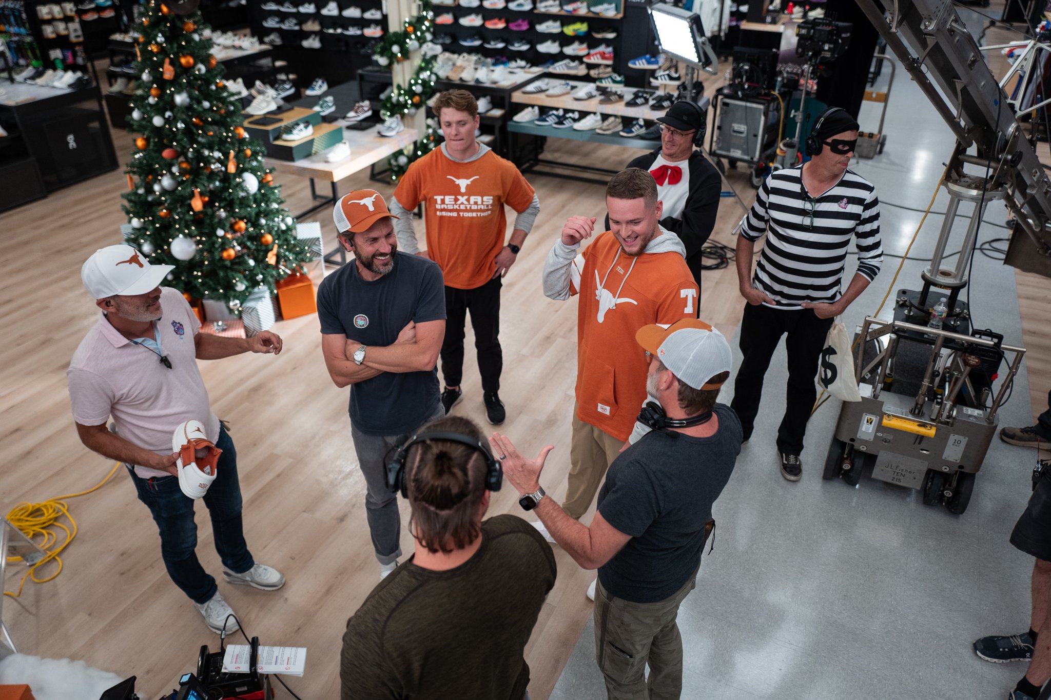 Group of people, including some wearing orange Texas Longhorns shirts, having a conversation in a retail store decorated for Christmas, with a Christmas tree in the background.