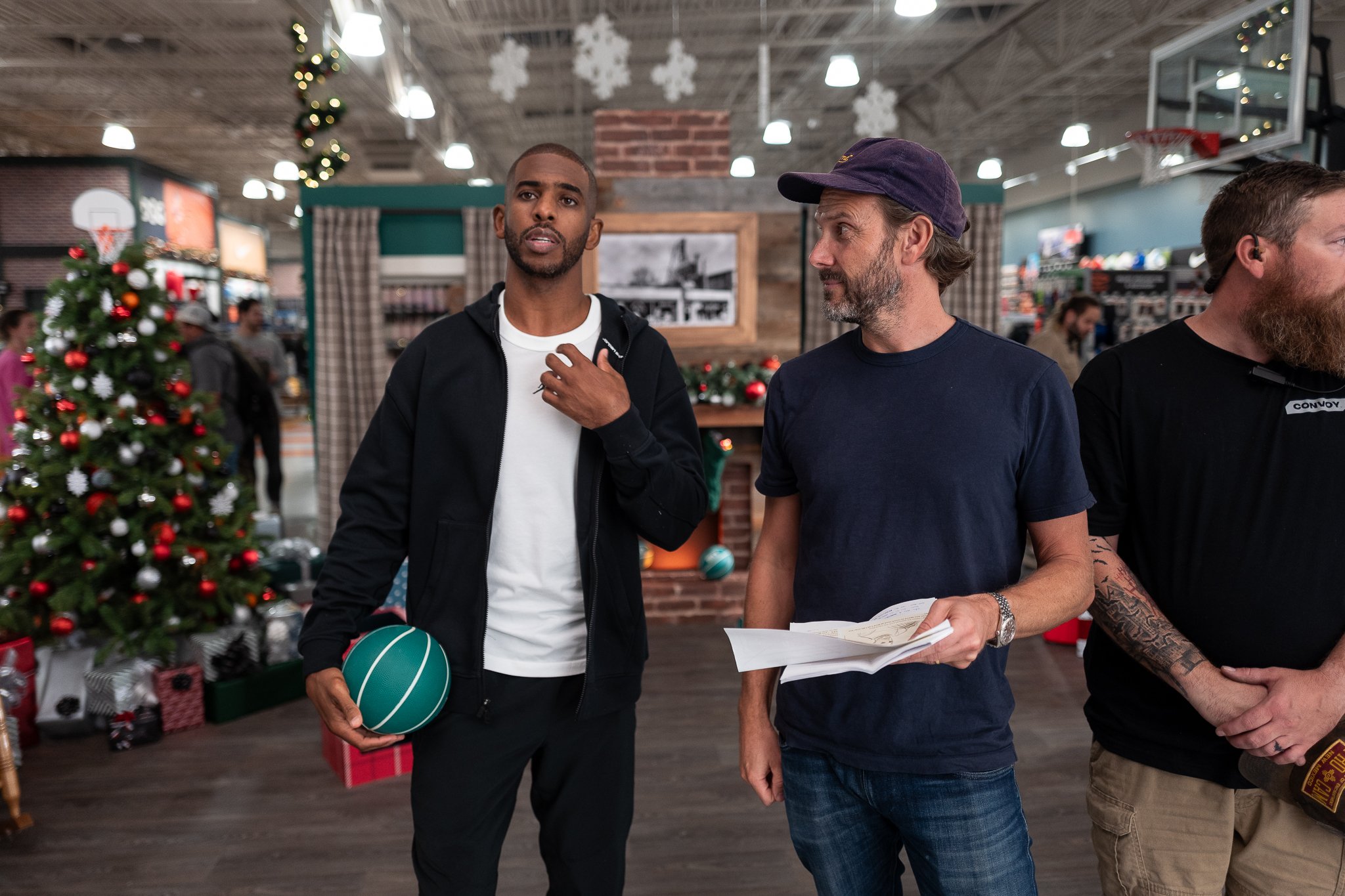 Three men standing in a store decorated for Christmas, with a Christmas tree, ornaments, and snowflake decorations hanging from the ceiling.