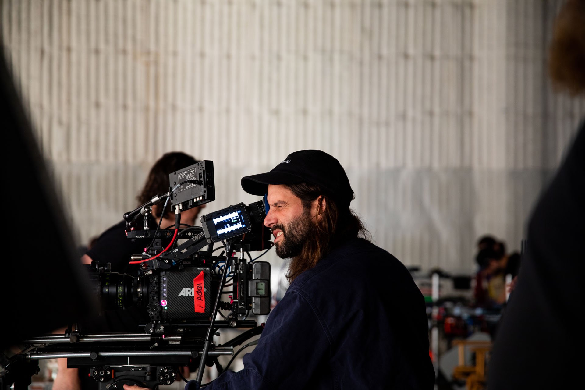 A filmmaker operating a professional ARRI camera on a film set, with crew members and equipment in the background.