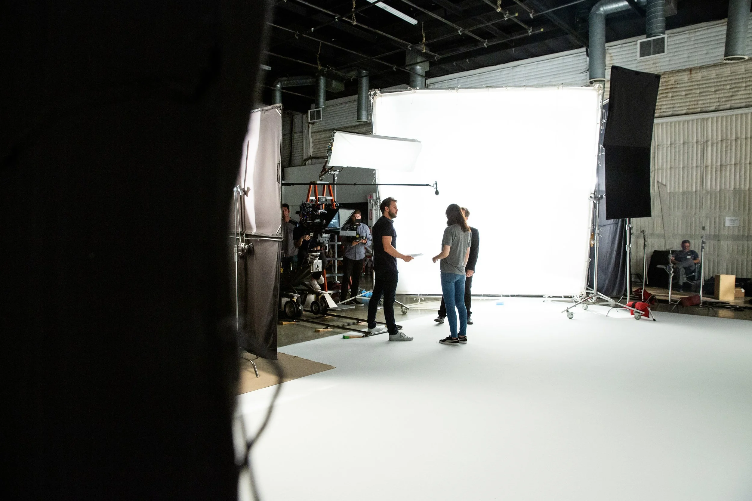 Film crew setting up a white backdrop and lighting in a studio for filming or photography.