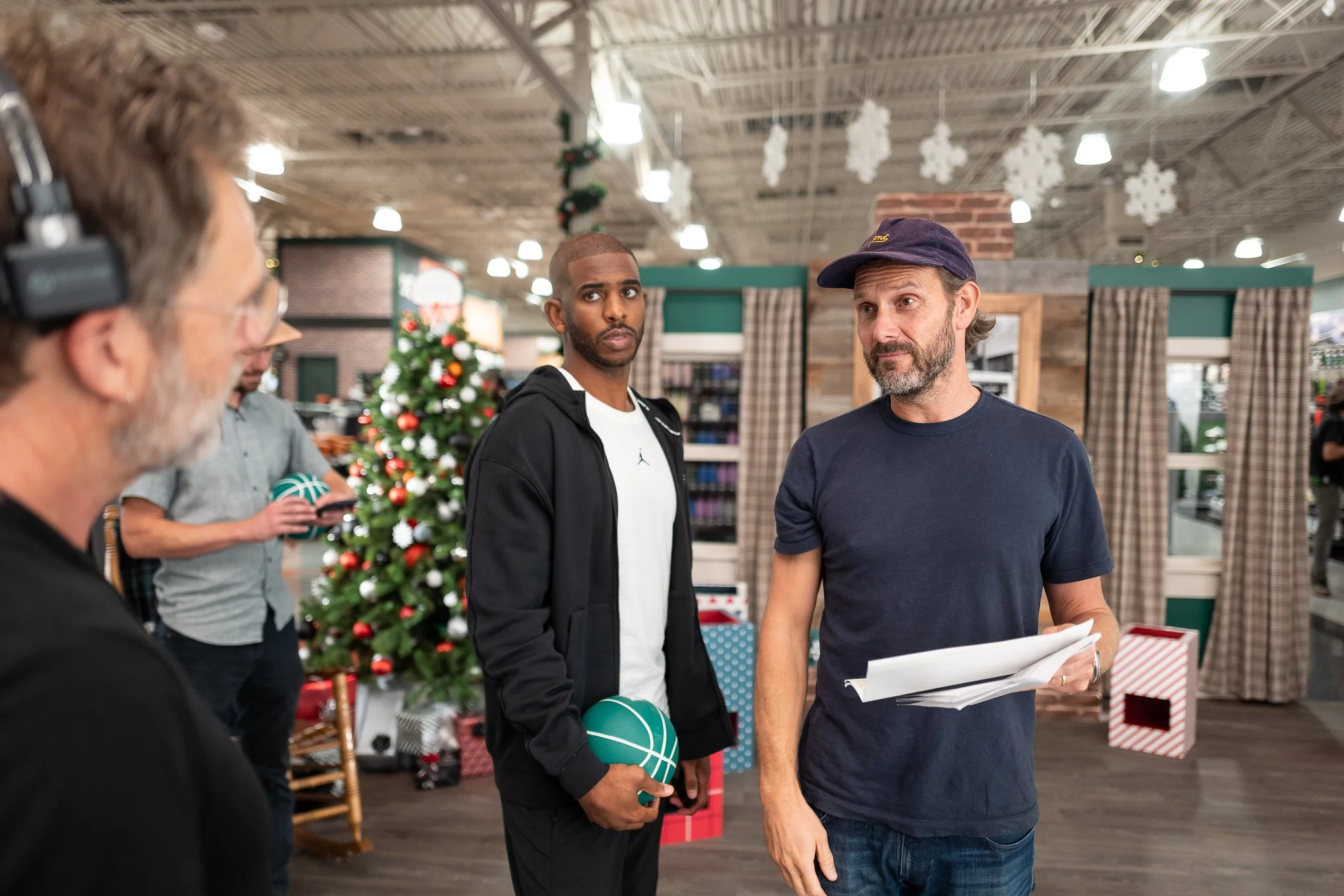 Group of men talking in a store decorated for Christmas, with a Christmas tree and holiday decorations in the background.