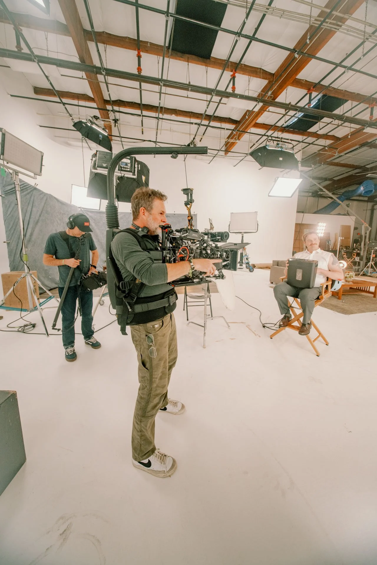 Film production crew filming a man using a laptop on a chair in a studio with lighting equipment.