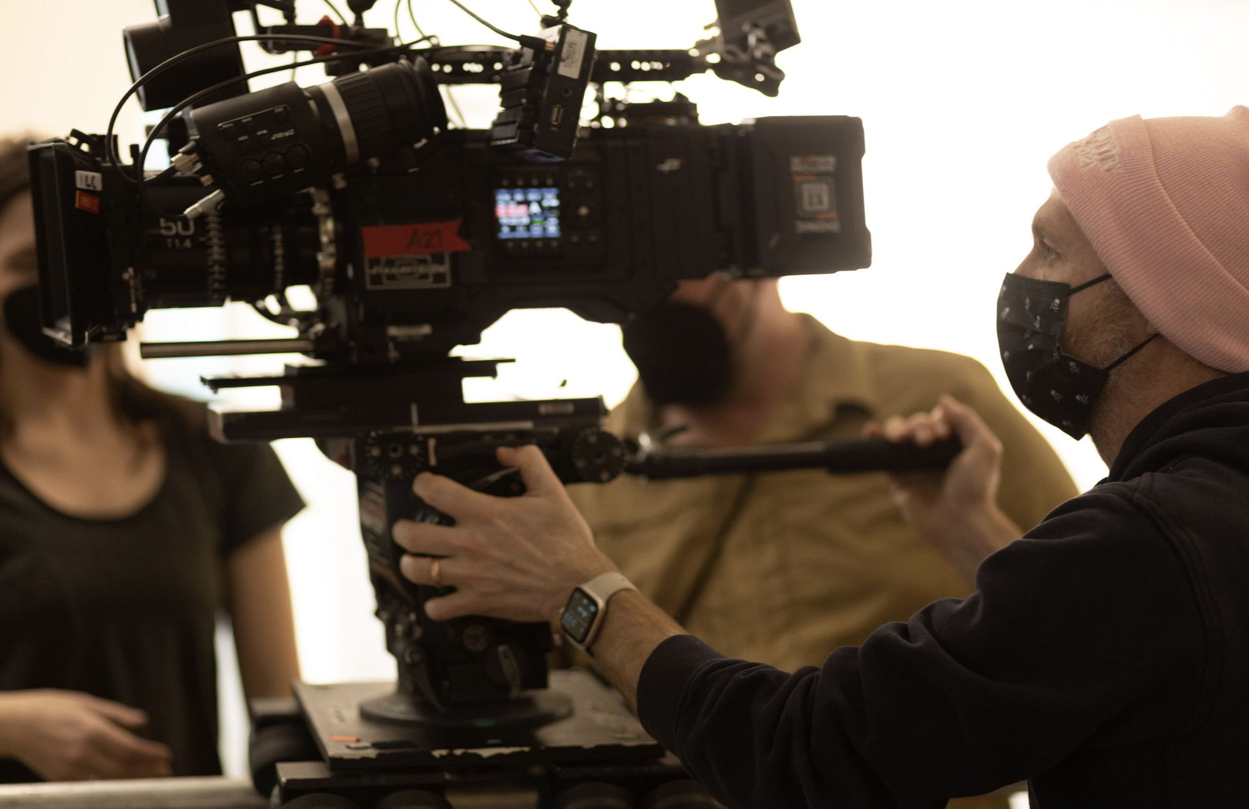 Person with a pink beanie and face mask operating a professional video camera on a stabilizer.