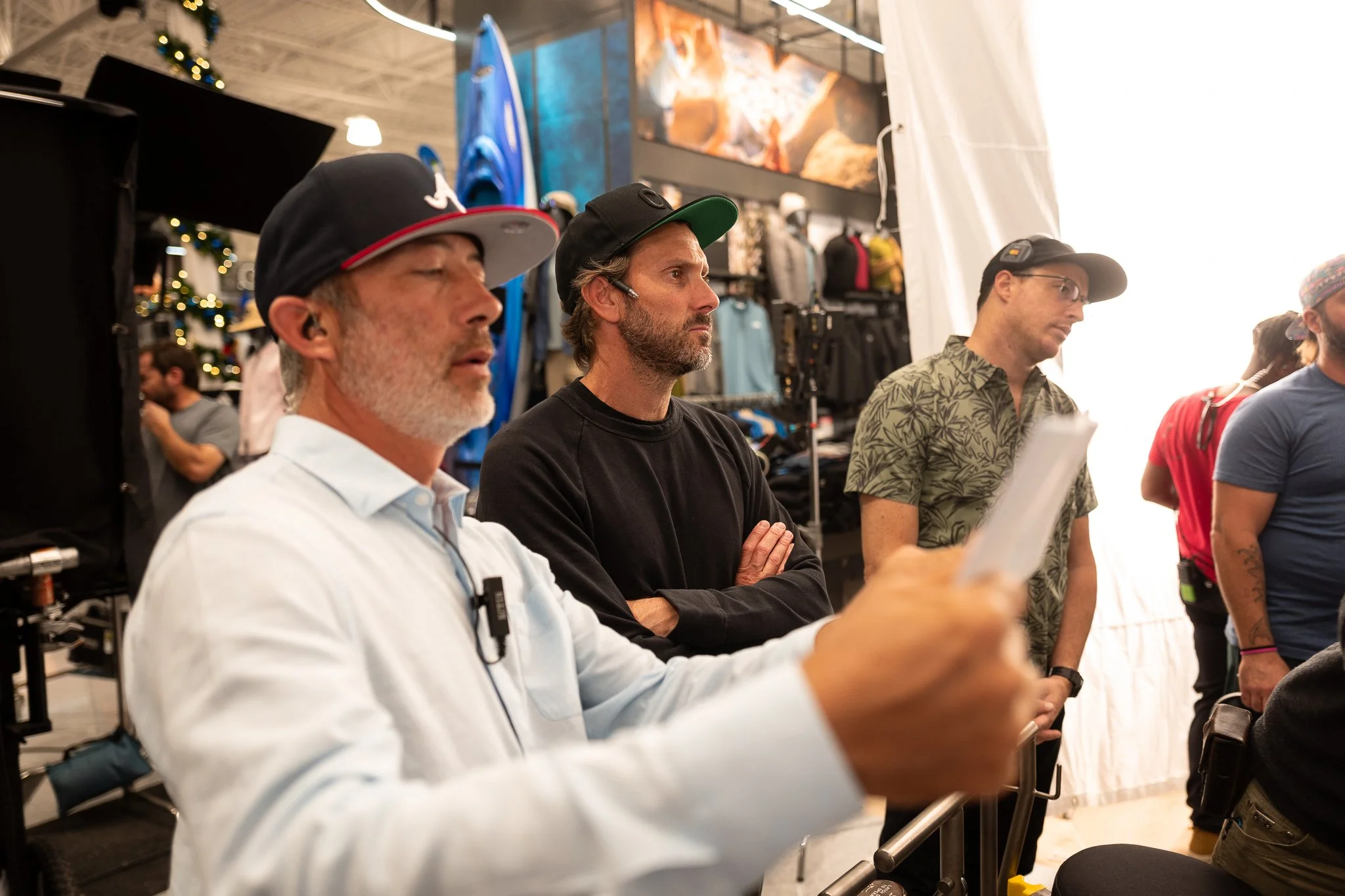Group of men standing inside a store with outdoor gear and clothing, some wearing hats or glasses, engaged in an event or presentation.