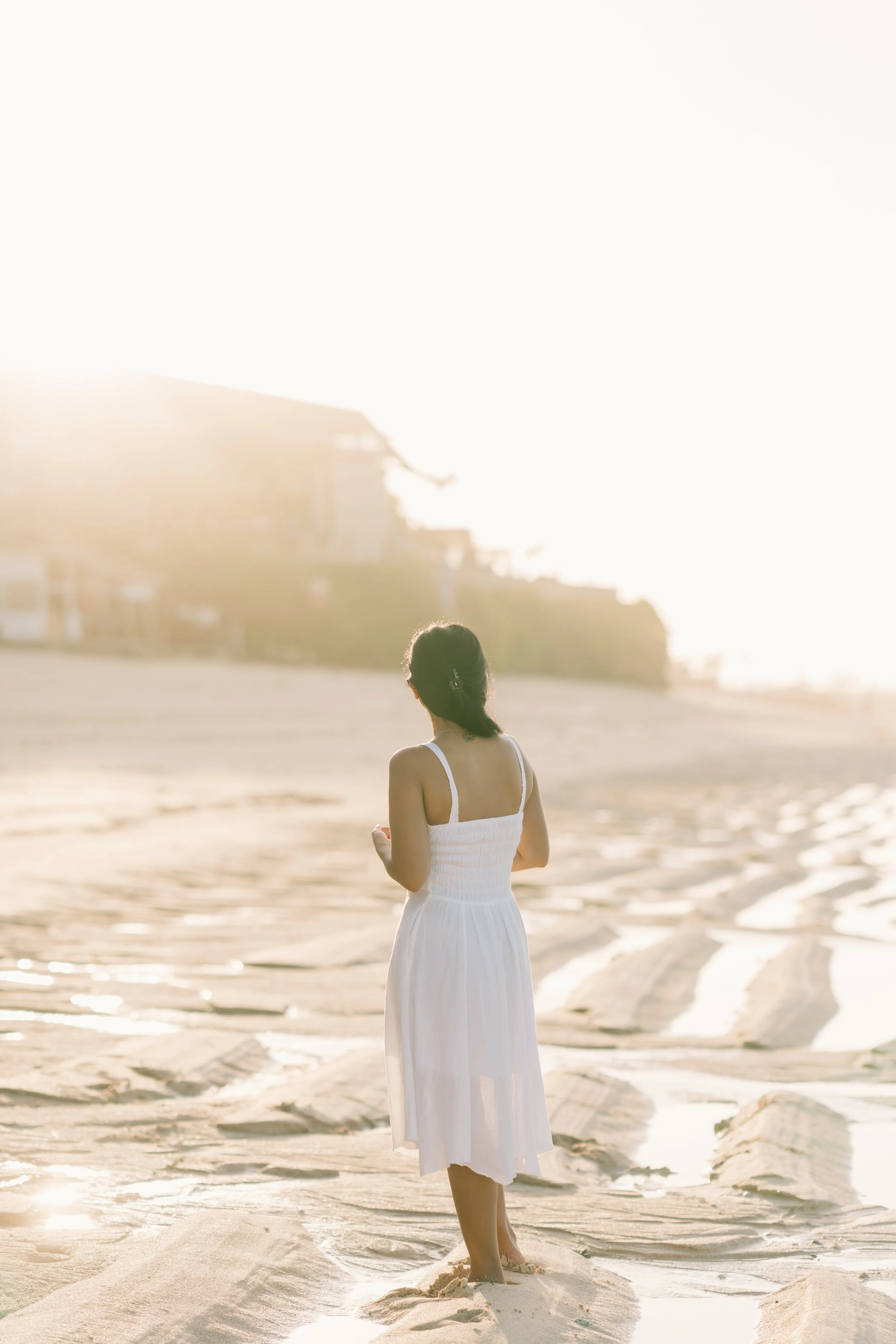 A woman in a white dress walking on the beach during sunset.