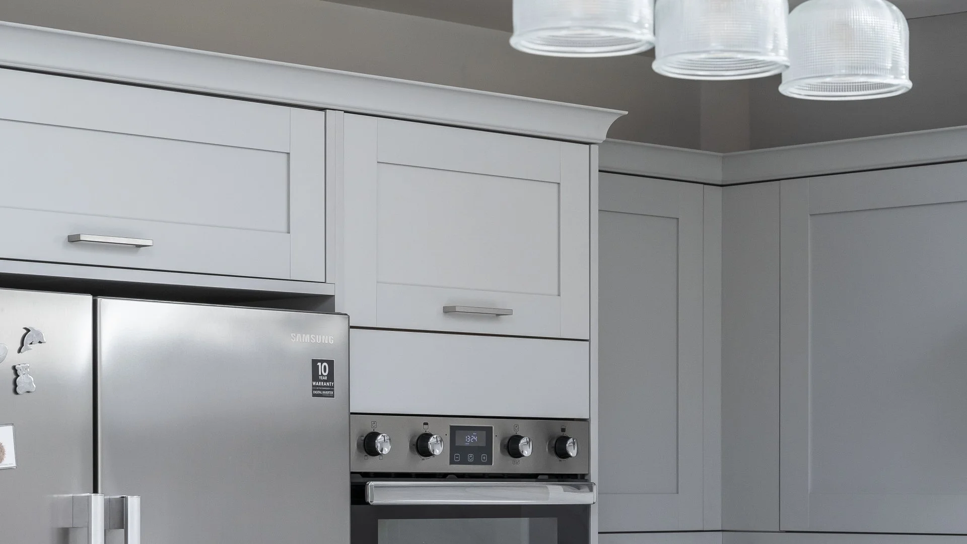 Close-up of a modern kitchen with white cabinets, stainless steel refrigerator with magnets, and a stainless steel oven with knobs and a digital display.
