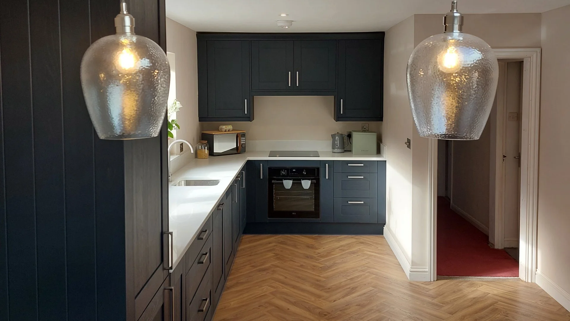 Modern kitchen with dark blue cabinets, white countertop, small appliances, and two hanging glass pendant lights.