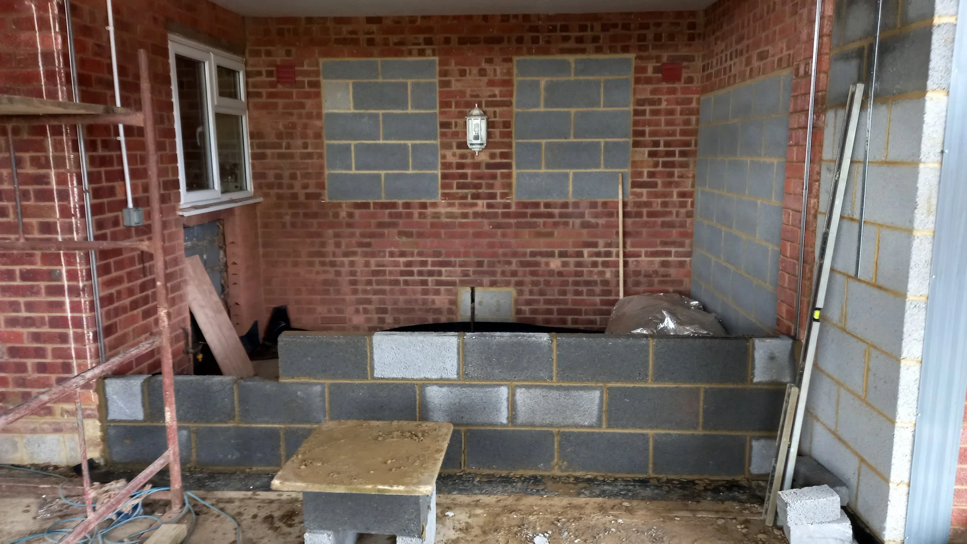 Construction site showing brick walls and concrete blocks with a window, a ladder, and construction materials.