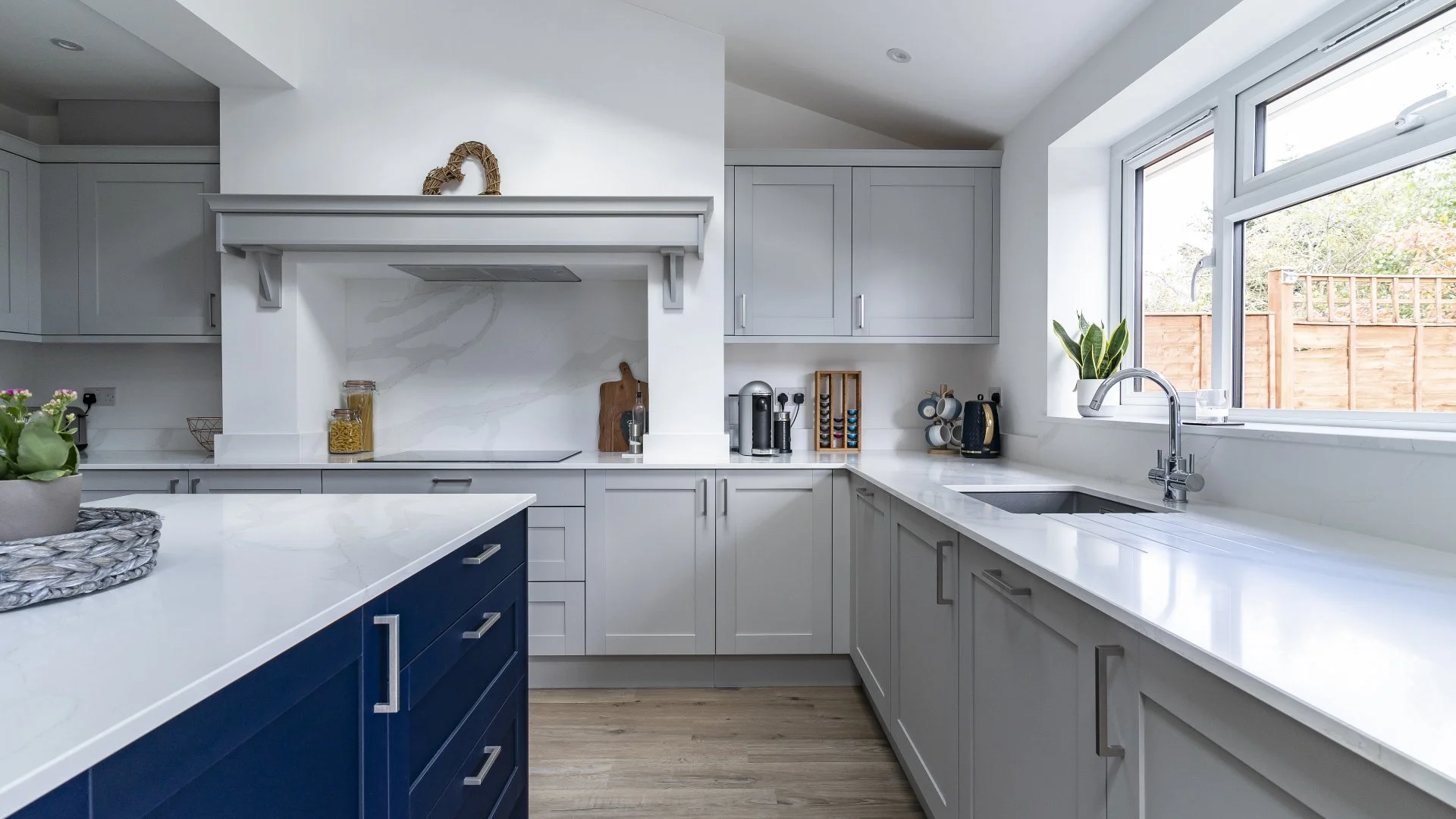 Modern kitchen with white cabinets, a navy blue kitchen island, a marble backsplash, and a large window showing a backyard fence.