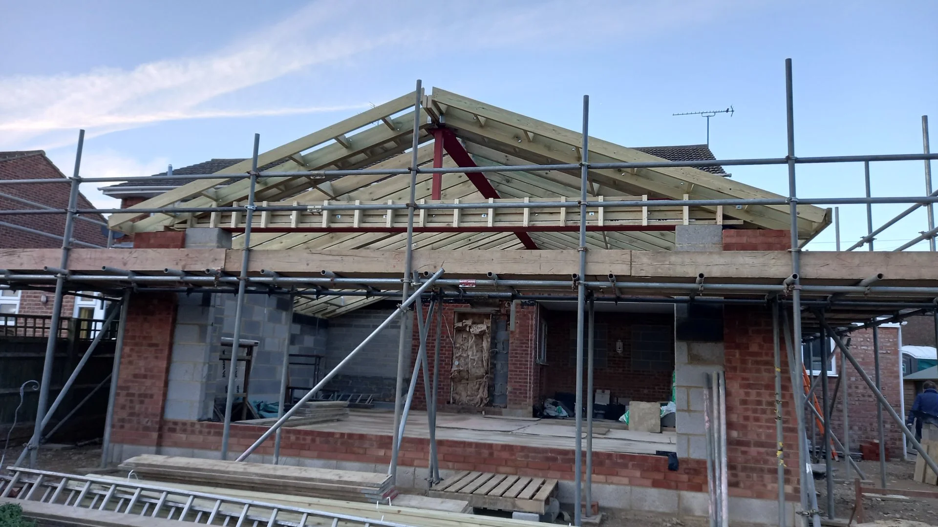 Construction site of a house with scaffolding and an incomplete roof structure made of wooden beams.