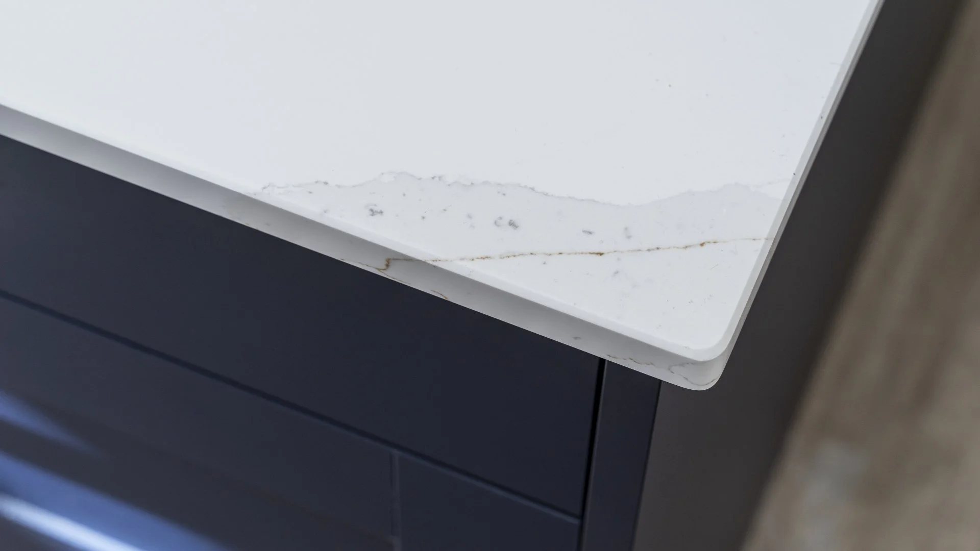 Close-up of a white marble countertop with subtle gray and brown veining, attached to a dark-colored cabinet.