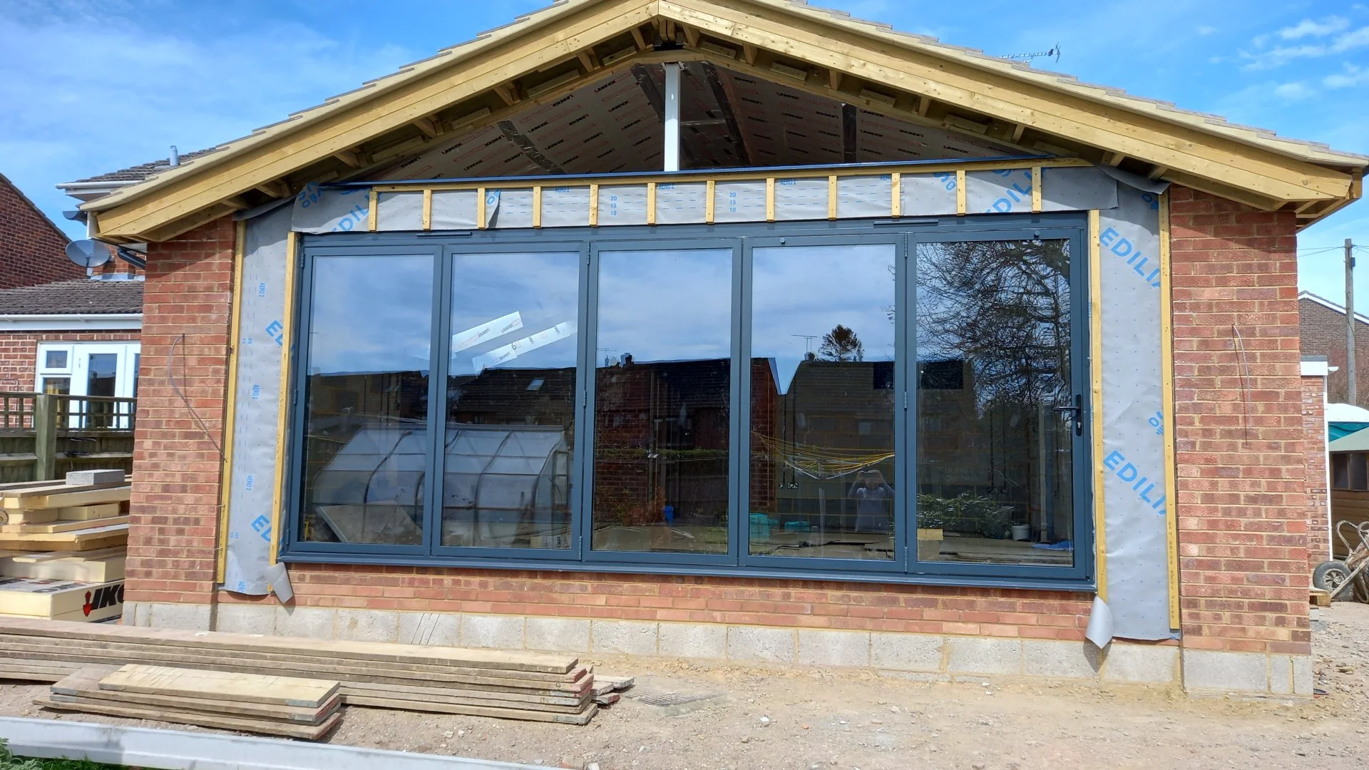 Construction of a brick house extension with large glass doors and a new roof being added.