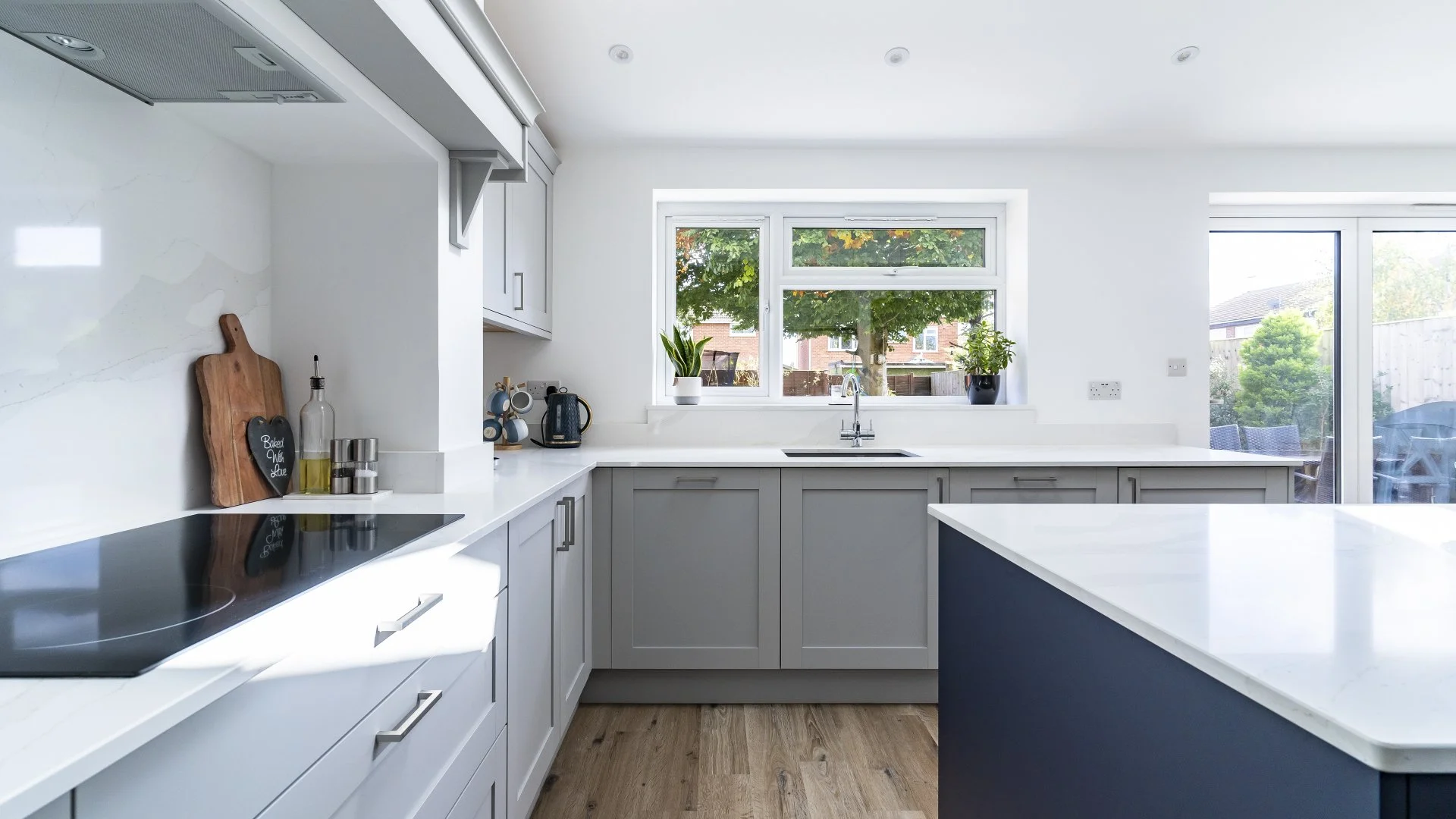 Modern kitchen with white cabinets, a black stovetop, and a large window with green trees outside.