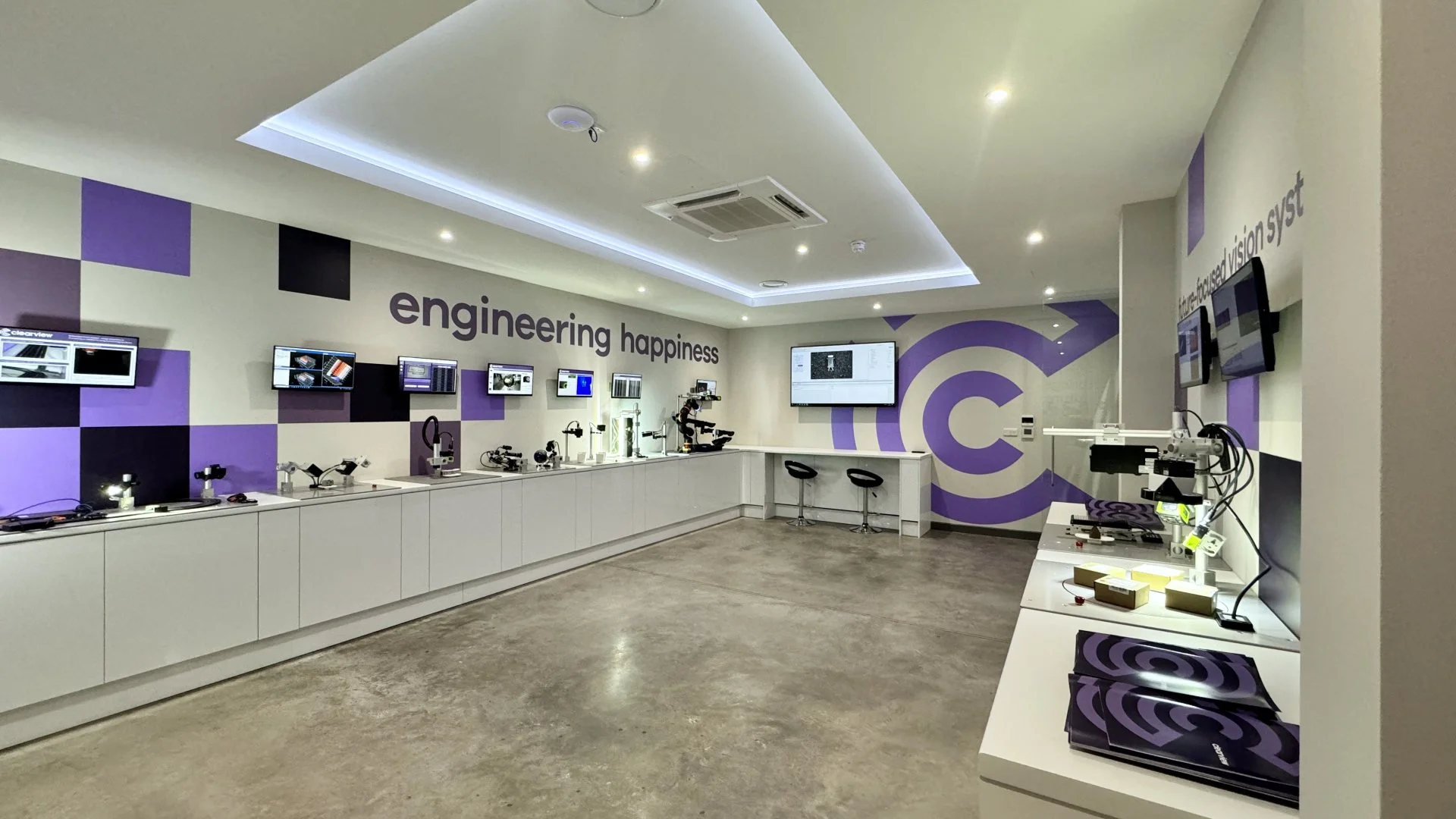 Modern technology exhibit room with microscopes and digital displays, featuring the words 'engineering happiness' on the wall.