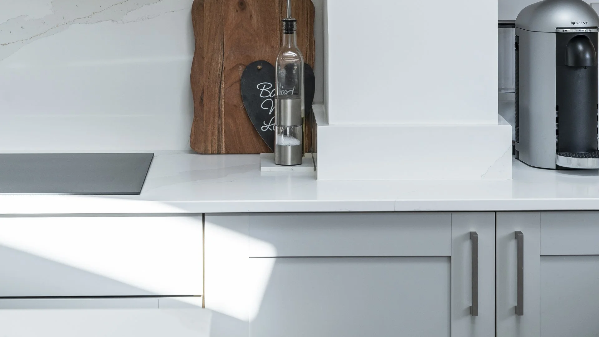 Modern kitchen countertop with a soap dispenser, a wooden cutting board, and a coffee machine, with bright natural light.