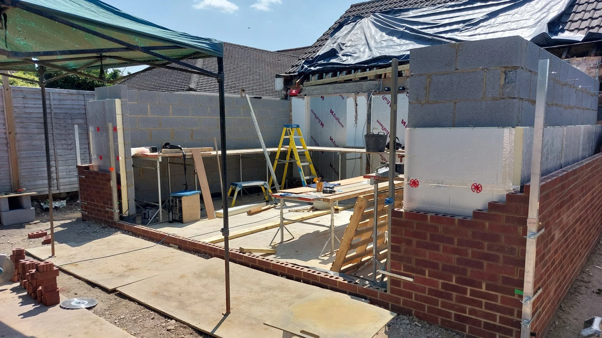 Construction site with brick walls, scaffolding, ladders, and building materials during construction.