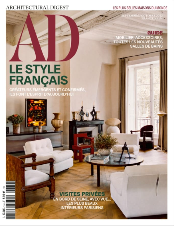 Page de magazine montrant un salon élégant avec des meubles en style français, un feu ouvert, des plantes, et une grande fenêtre avec des rideaux.