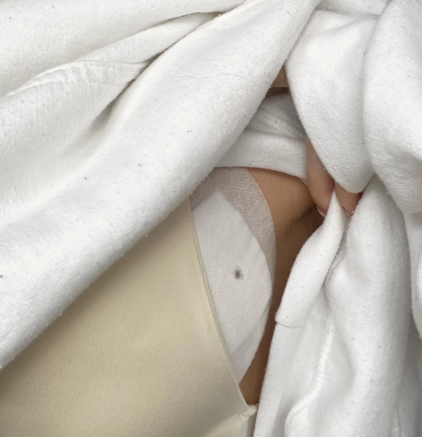 Close-up of a person wearing a white shirt and white hoodie, with the hoodie being pulled open to reveal their neck and collarbone area.