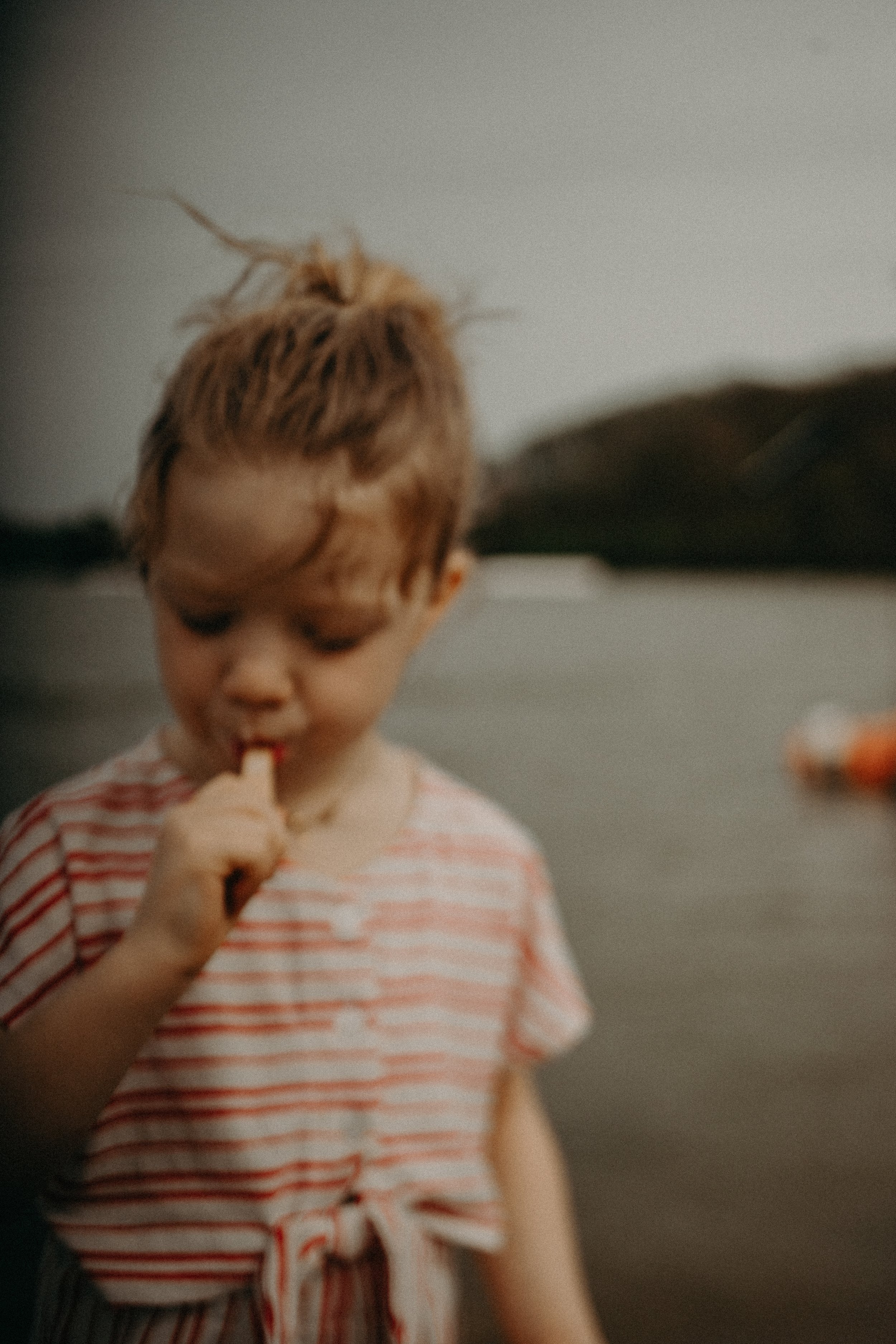 Un jeune garçon mange une glace près d'une étendue d'eau avec des montagnes en arrière-plan pendant le coucher du soleil.