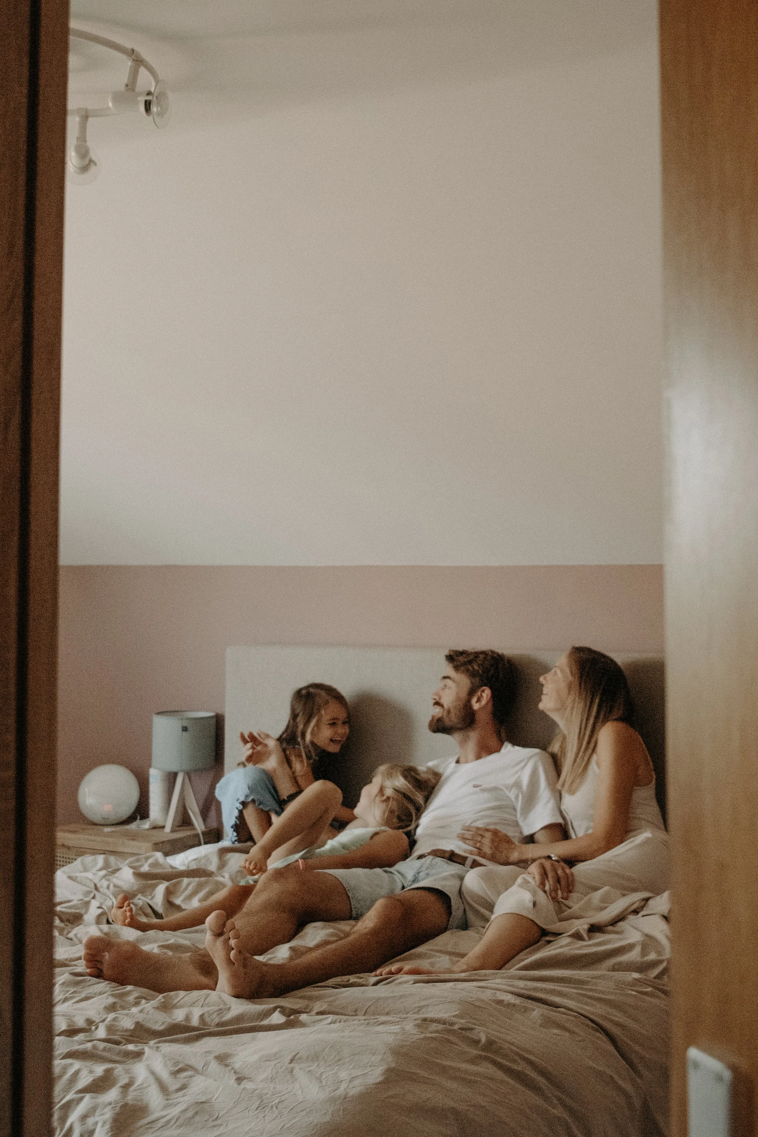 Une famille heureuse, composée d'un père, d'une mère et de deux filles, assise sur un lit dans une chambre chaleureuse et décorée de couleurs neutres