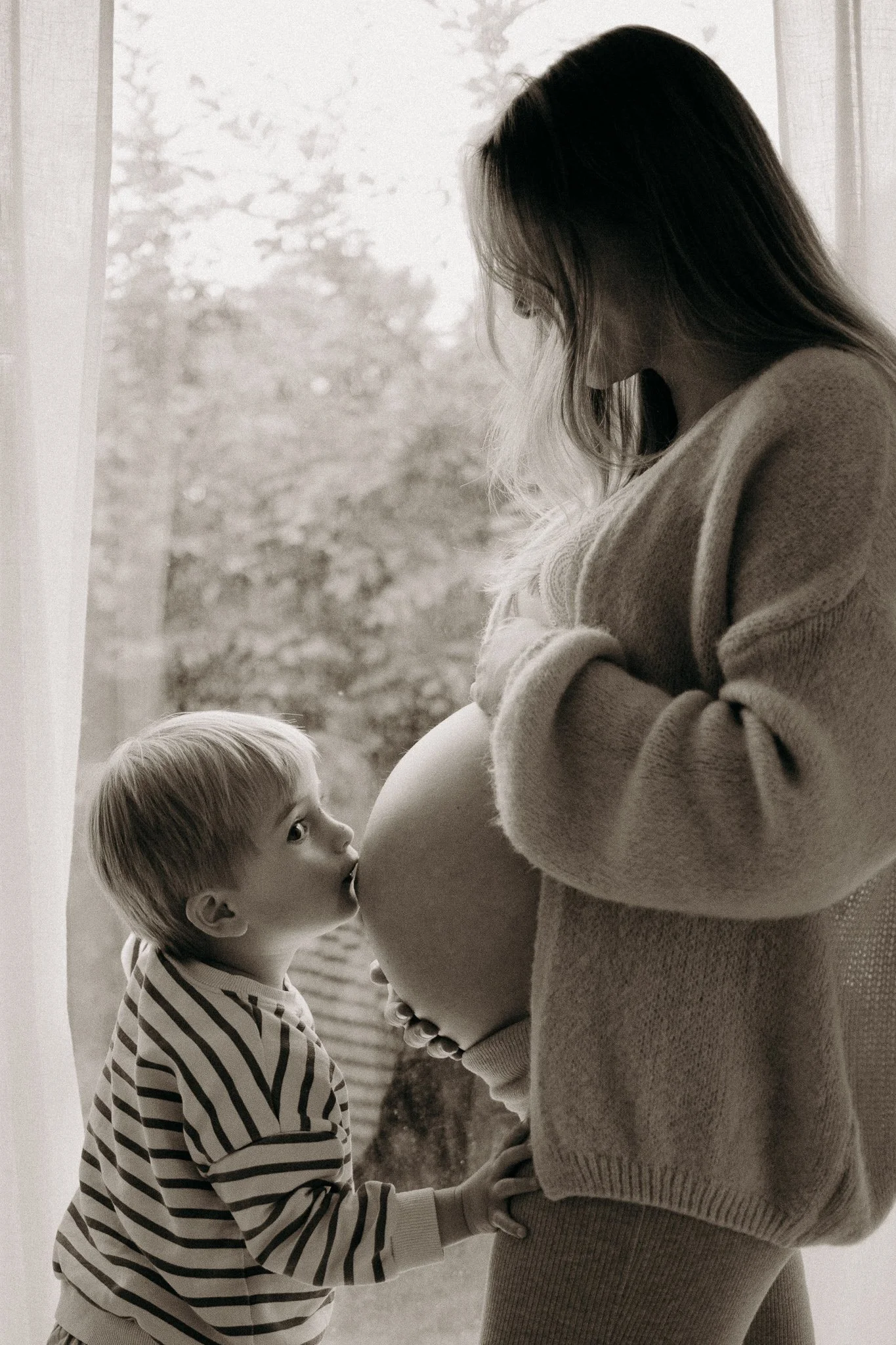 Une femme enceinte se tient près d'un enfant qui l'embrasse sur le ventre.