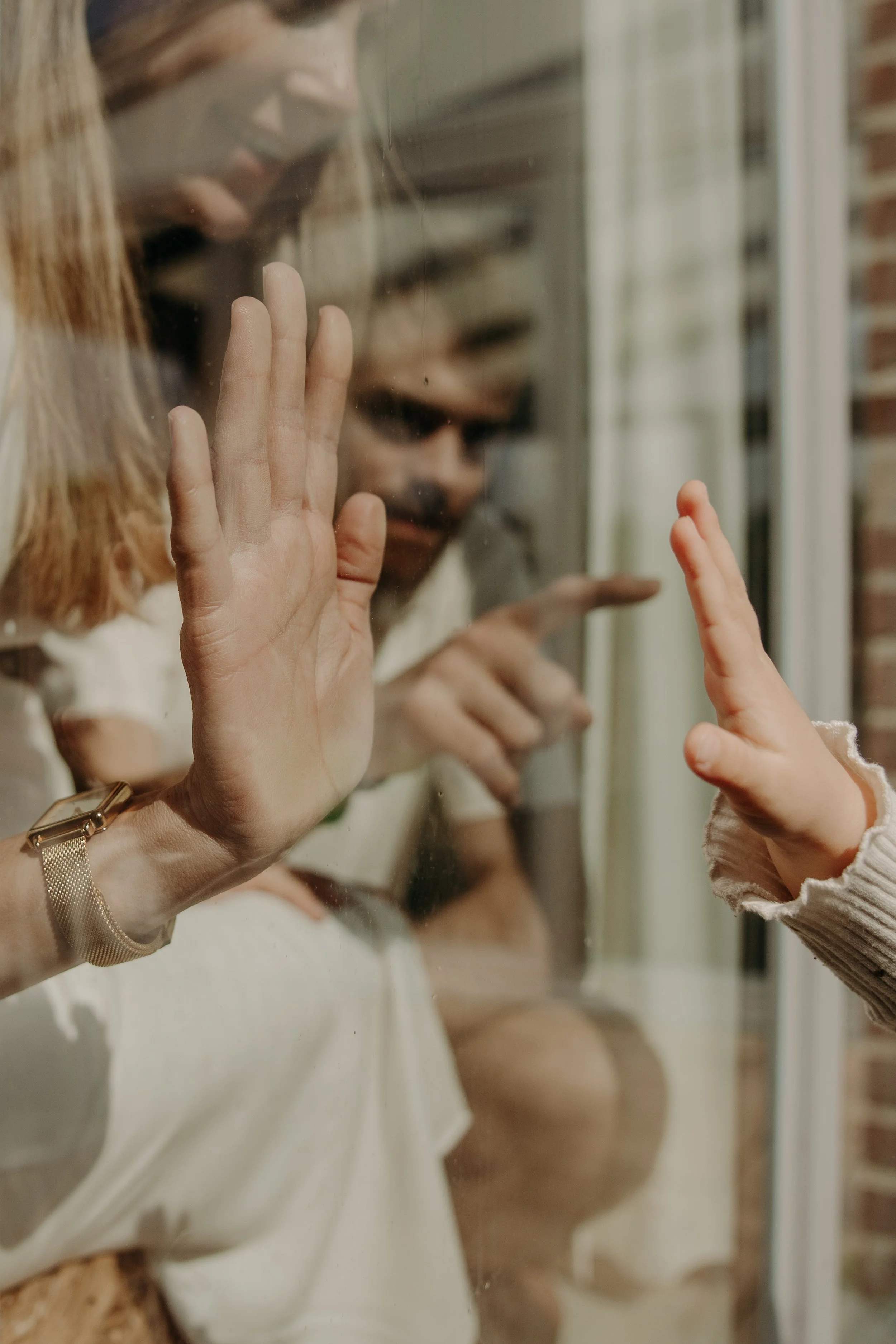 Une femme et un enfant pressent leurs mains contre une vitre, semblant se toucher ou communiquer à travers la vitre.