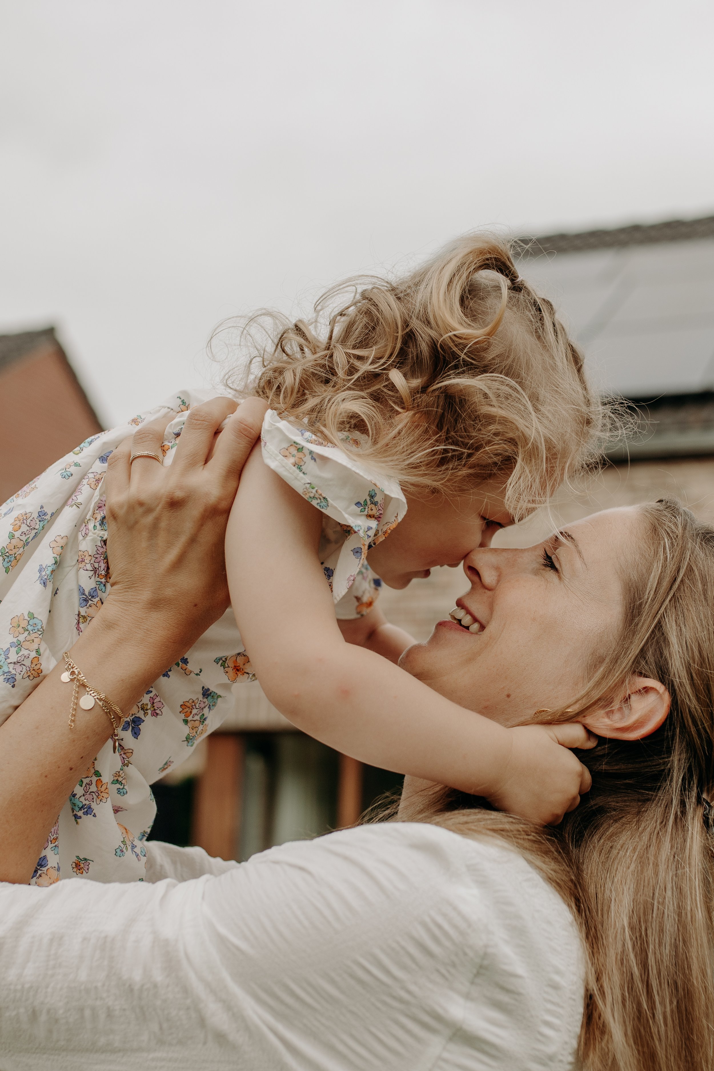 Une mère et sa fille jouent et s'embrassent, exprimant amour et joie en extérieur, avec un ciel nuageux en arrière-plan.