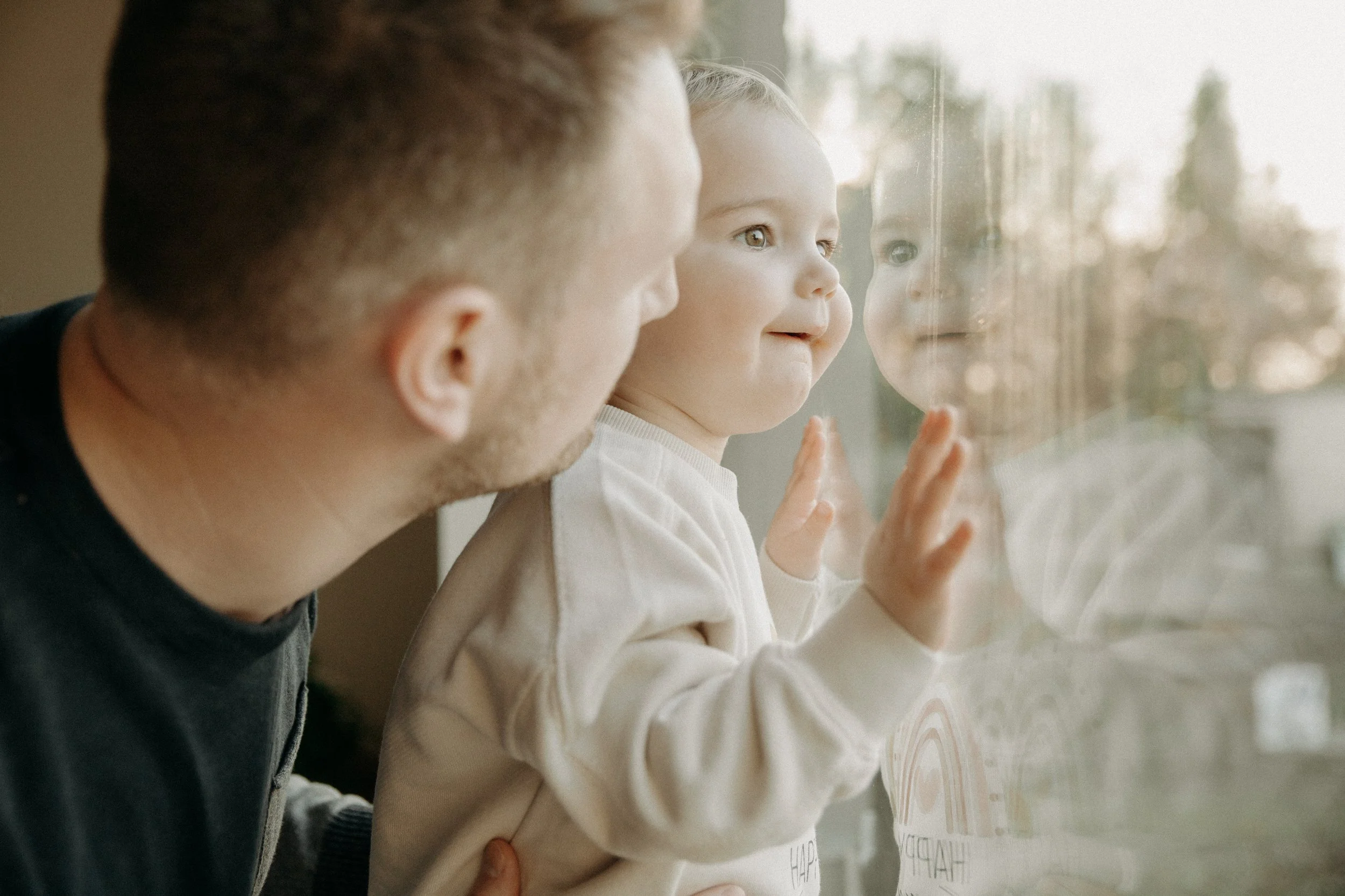 Un père et un enfant regardant à travers une vitre, l'enfant touche la vitre avec la main, et leur reflet est visible dans la vitre.