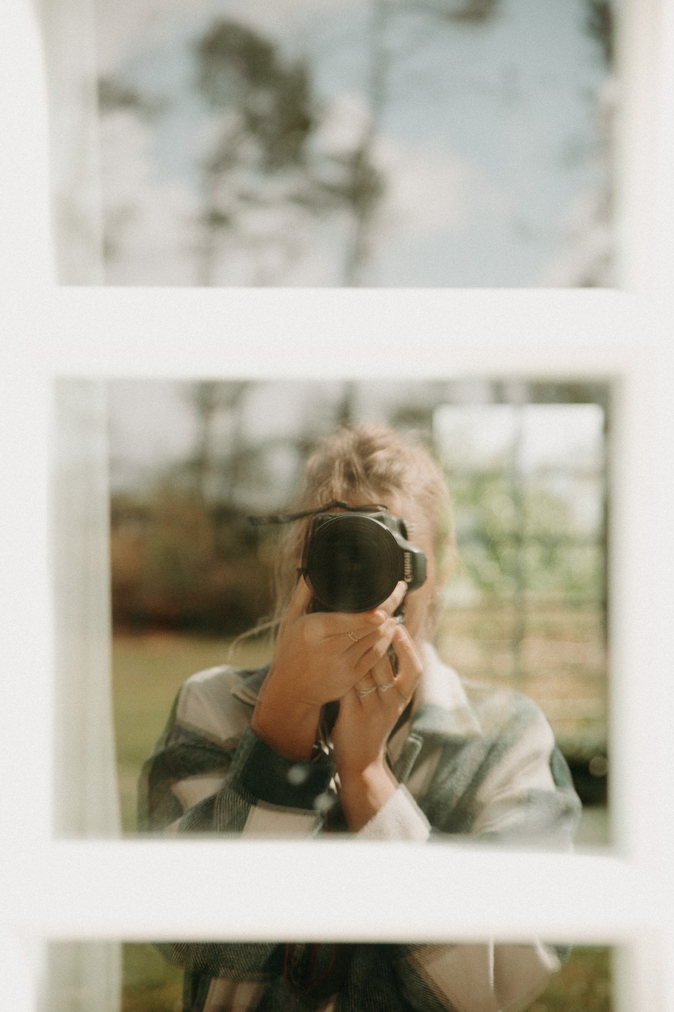 Une personne prenant une photo avec un appareil photo numérique, vue à travers une vitre avec plusieurs sections.