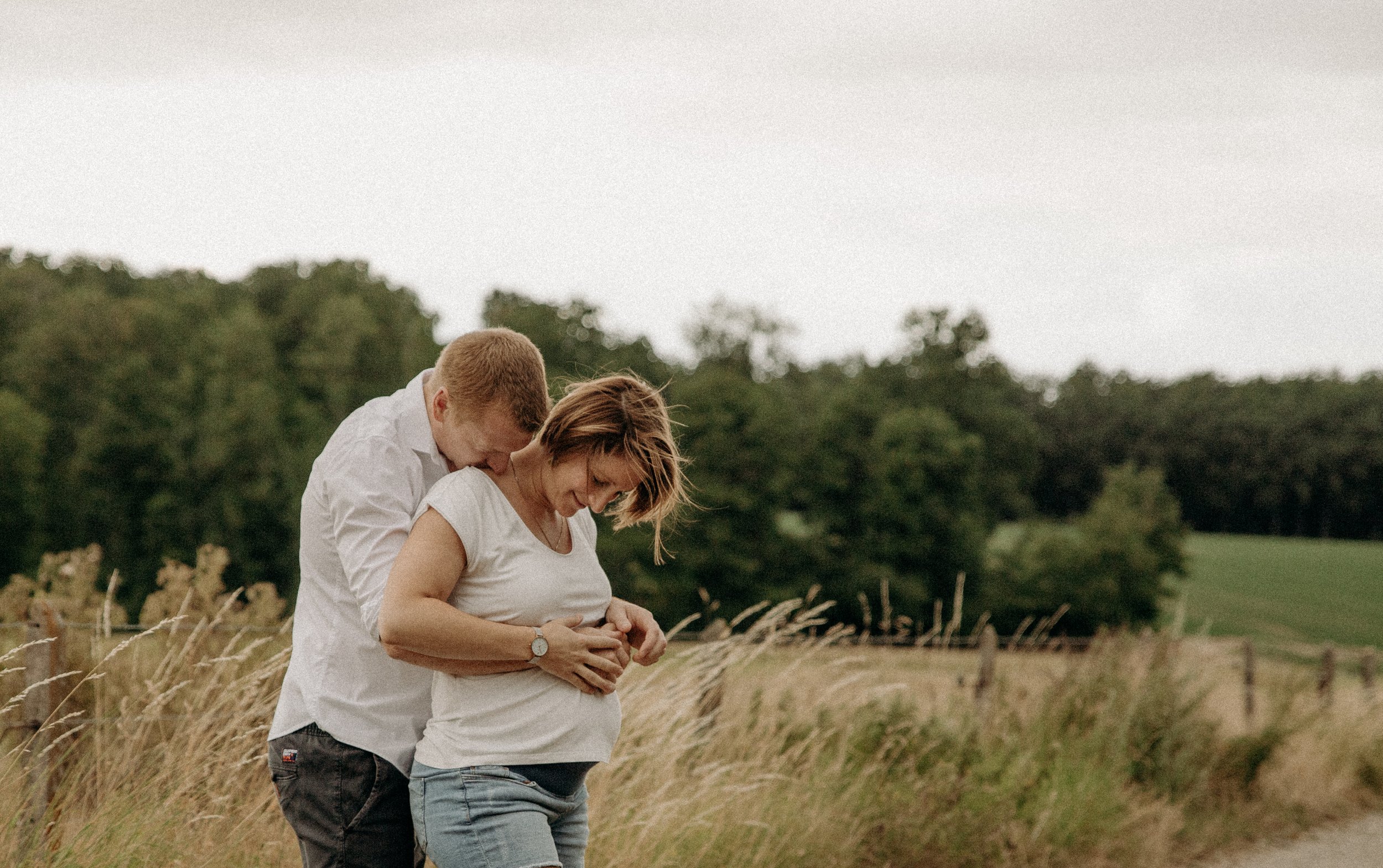 Un couple attend une grossesse dans un champ entouré de nature.