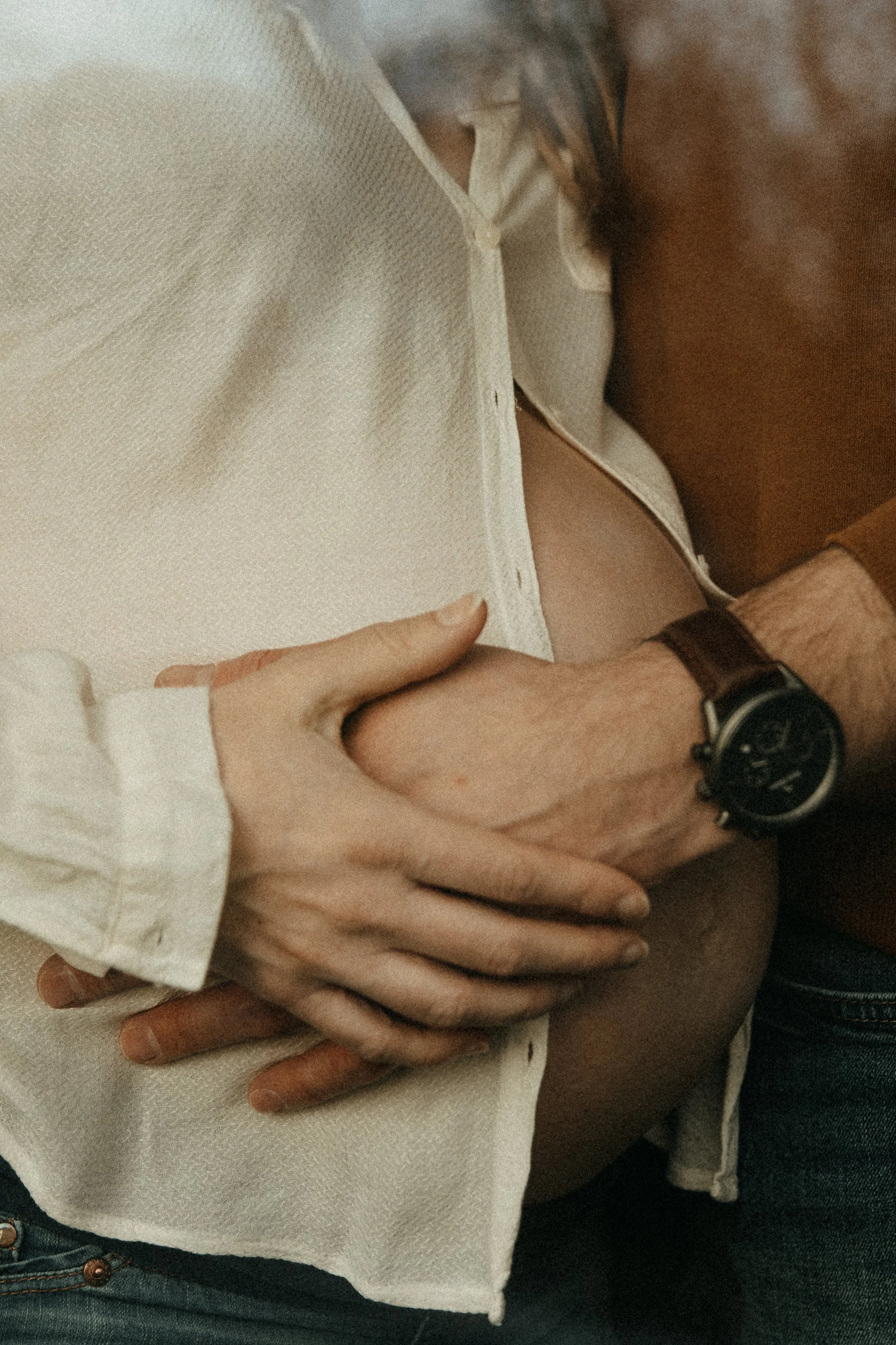 Deux personnes se tiennent par la main, avec un bras d'homme portant une montre en cuir et une femme avec une main posée sur sa cuisse, portant une chemise blanche.