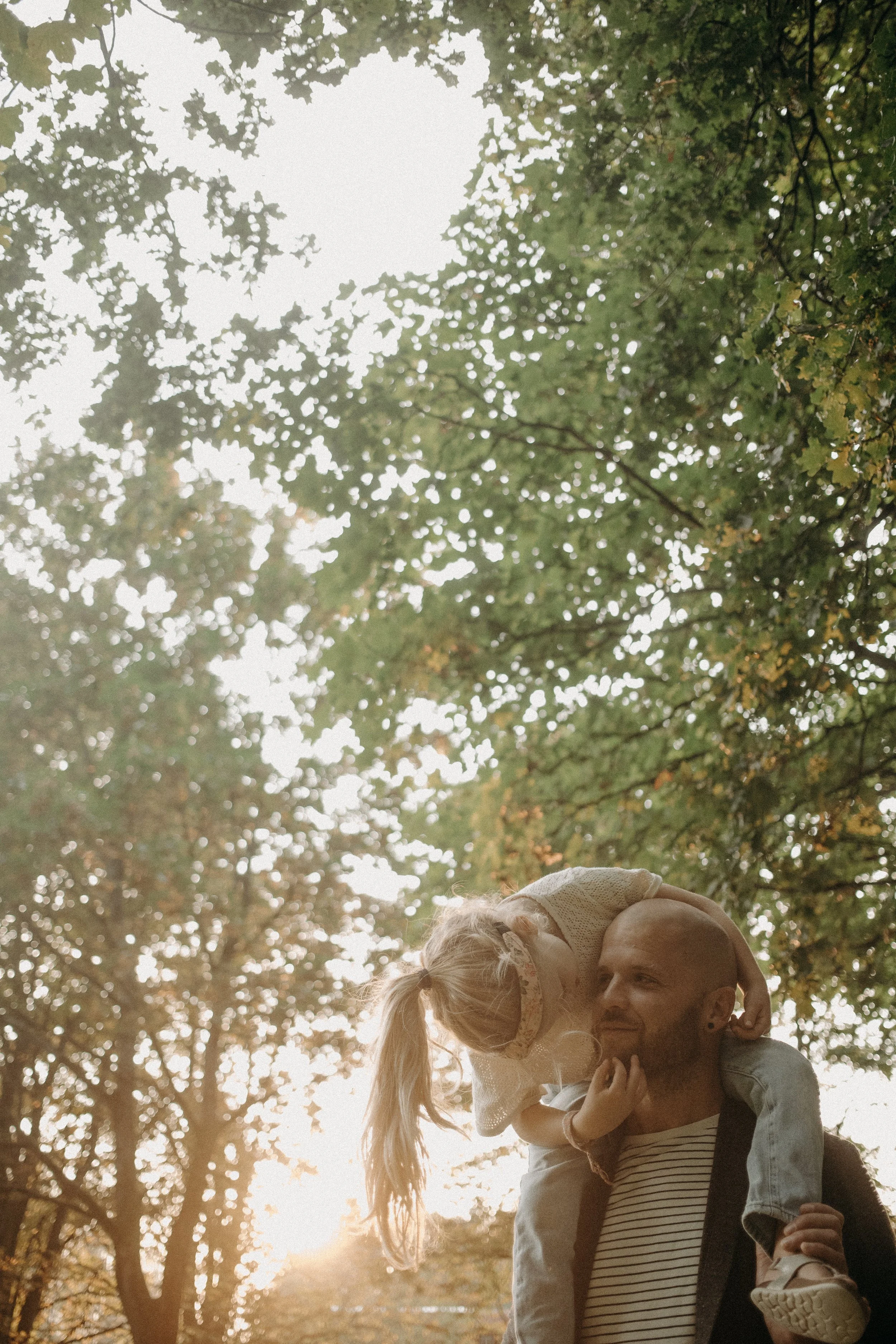 Un homme portant un t-shirt rayé est porté sur ses épaules par une femme dans un parc avec des arbres, au coucher du soleil.