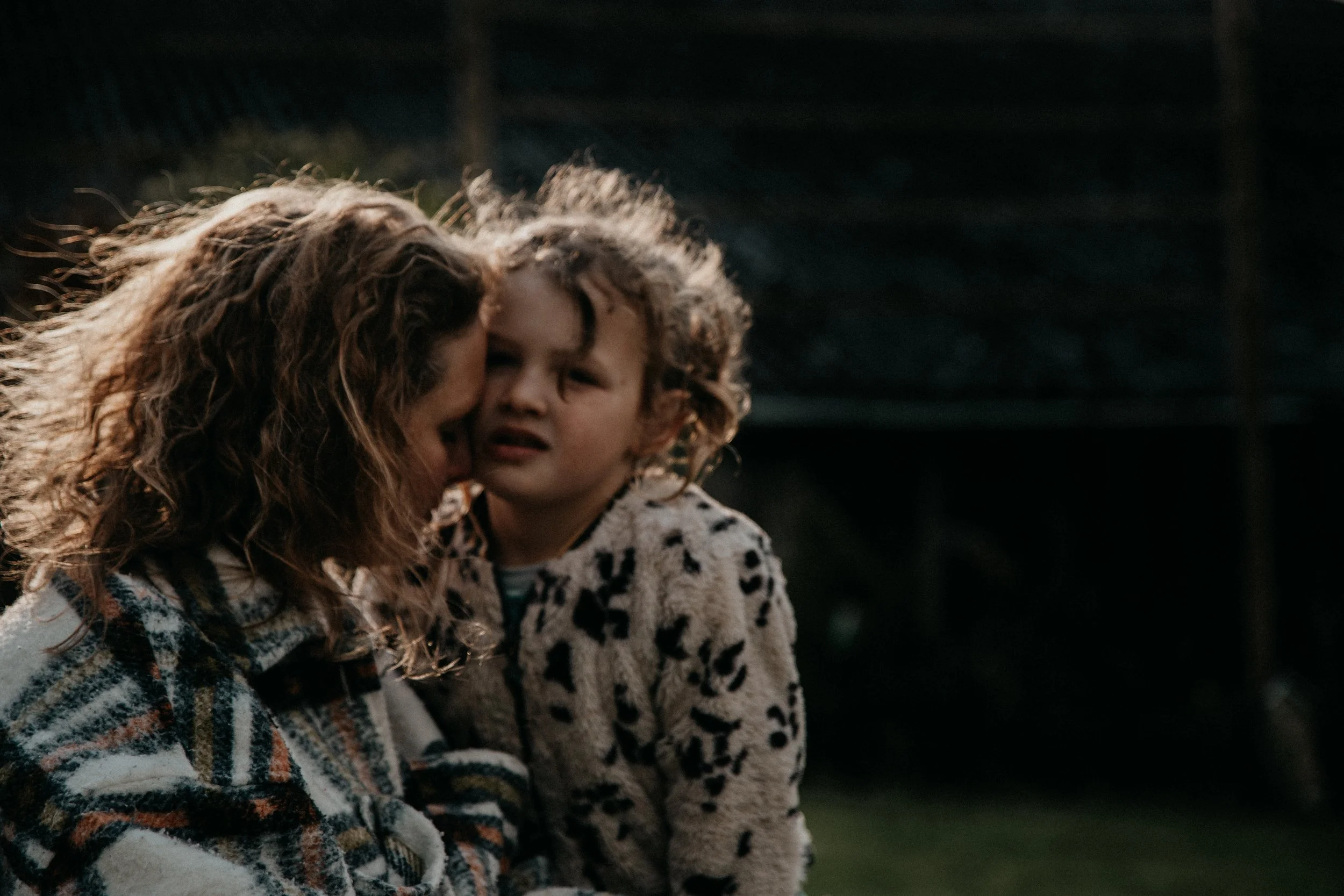 Une femme et un enfant ont une interaction émotionnelle, la femme cache son visage, et l'enfant regarde avec une expression confuse ou inquiète, en extérieur.