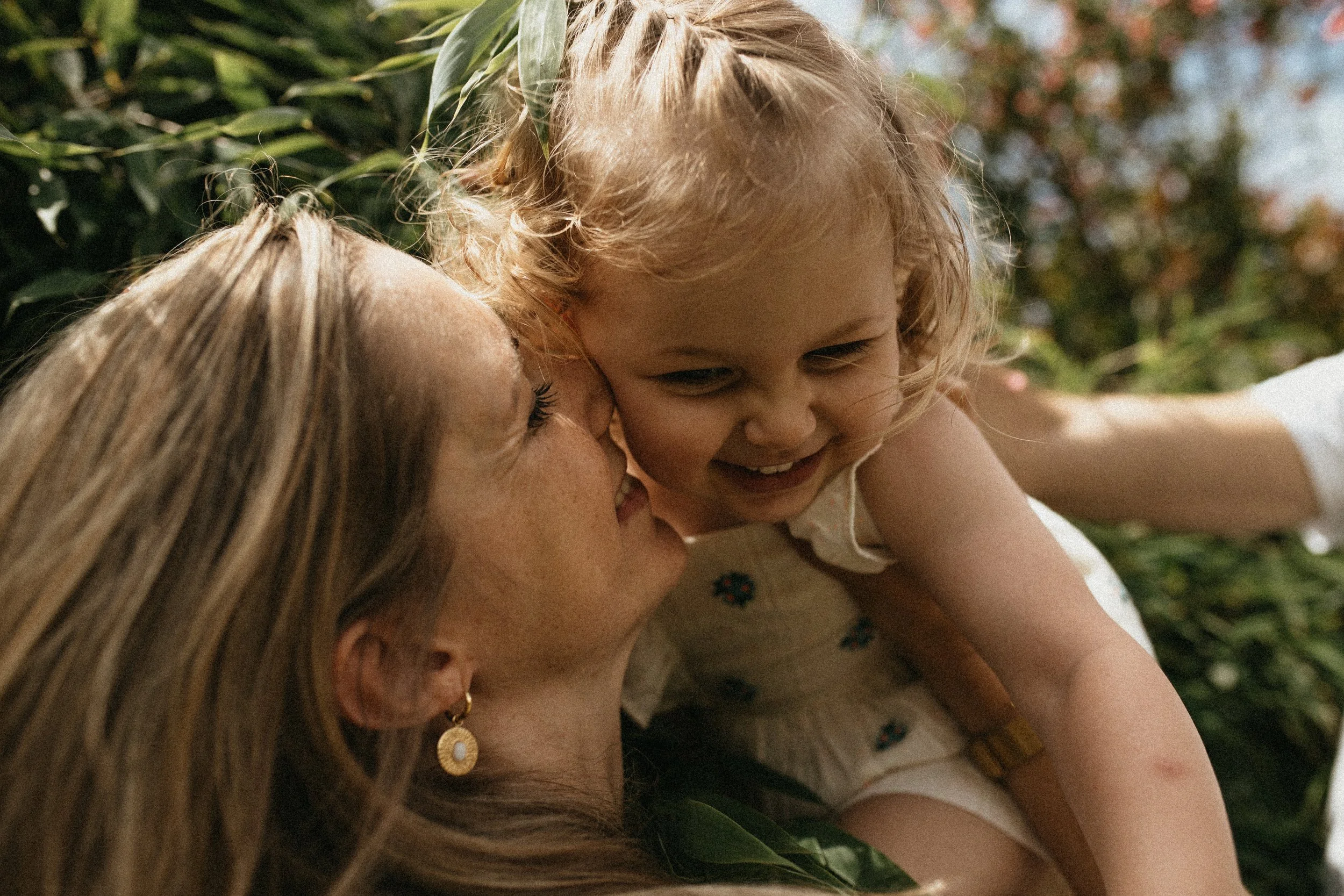 Une femme et une jeune fille jouent dans un environnement extérieur verdoyant, la femme regarde la jeune fille avec affection.