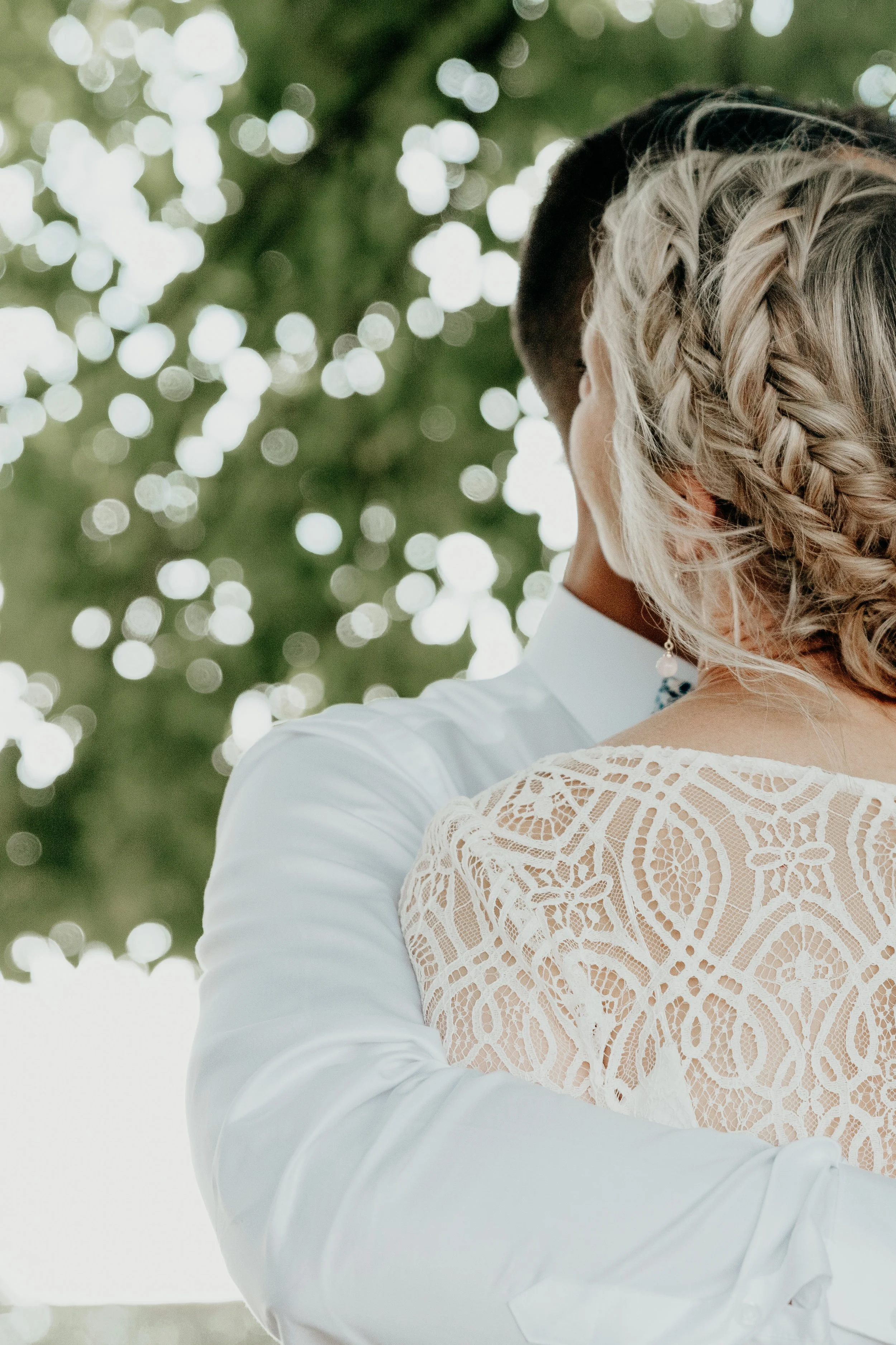 Un couple en costume de mariage s'embrassant à l'extérieur, avec des branches d'arbres floues en arrière-plan.