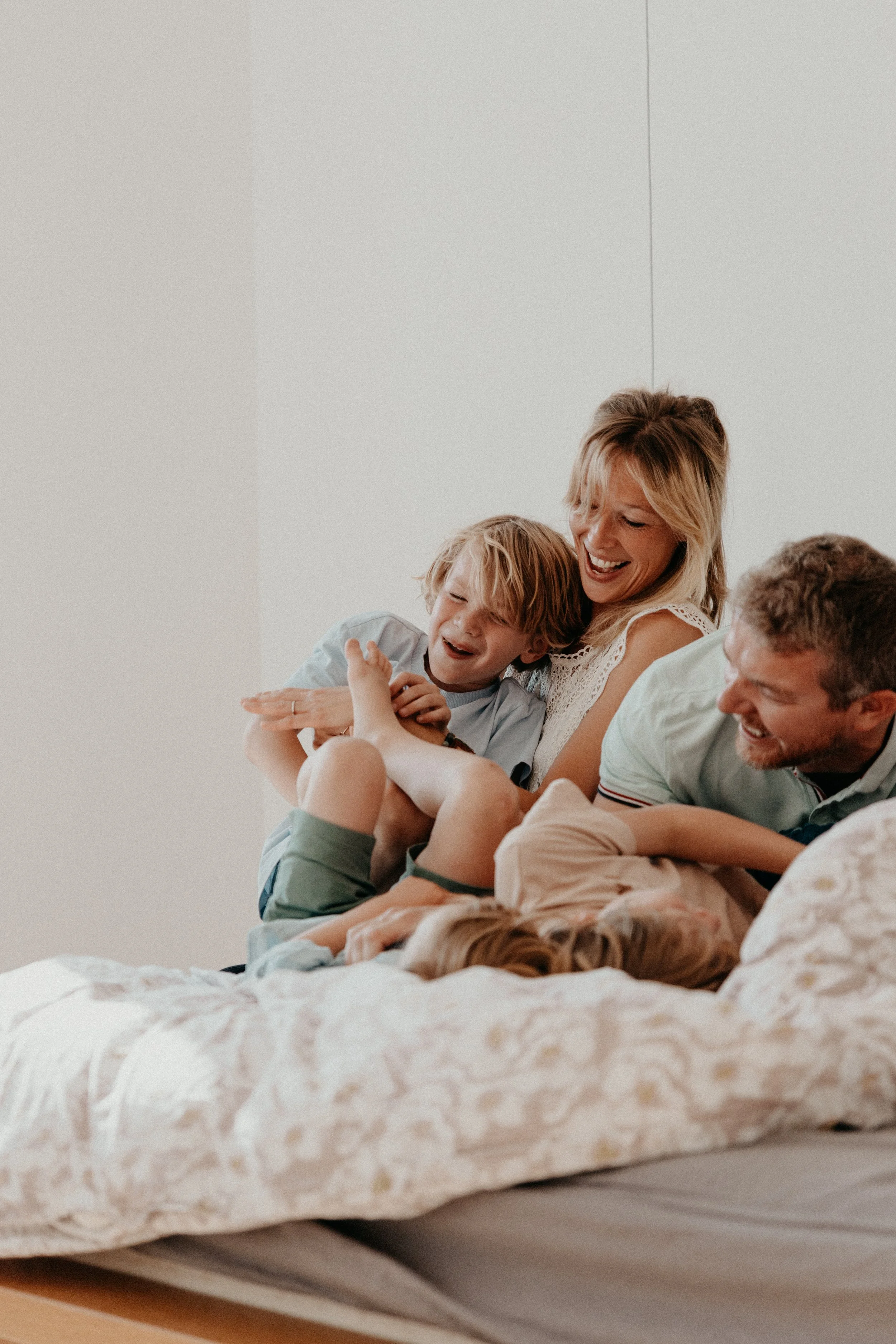Une famille riant et jouant sur un lit, composée d'un homme, d'une femme et de deux enfants