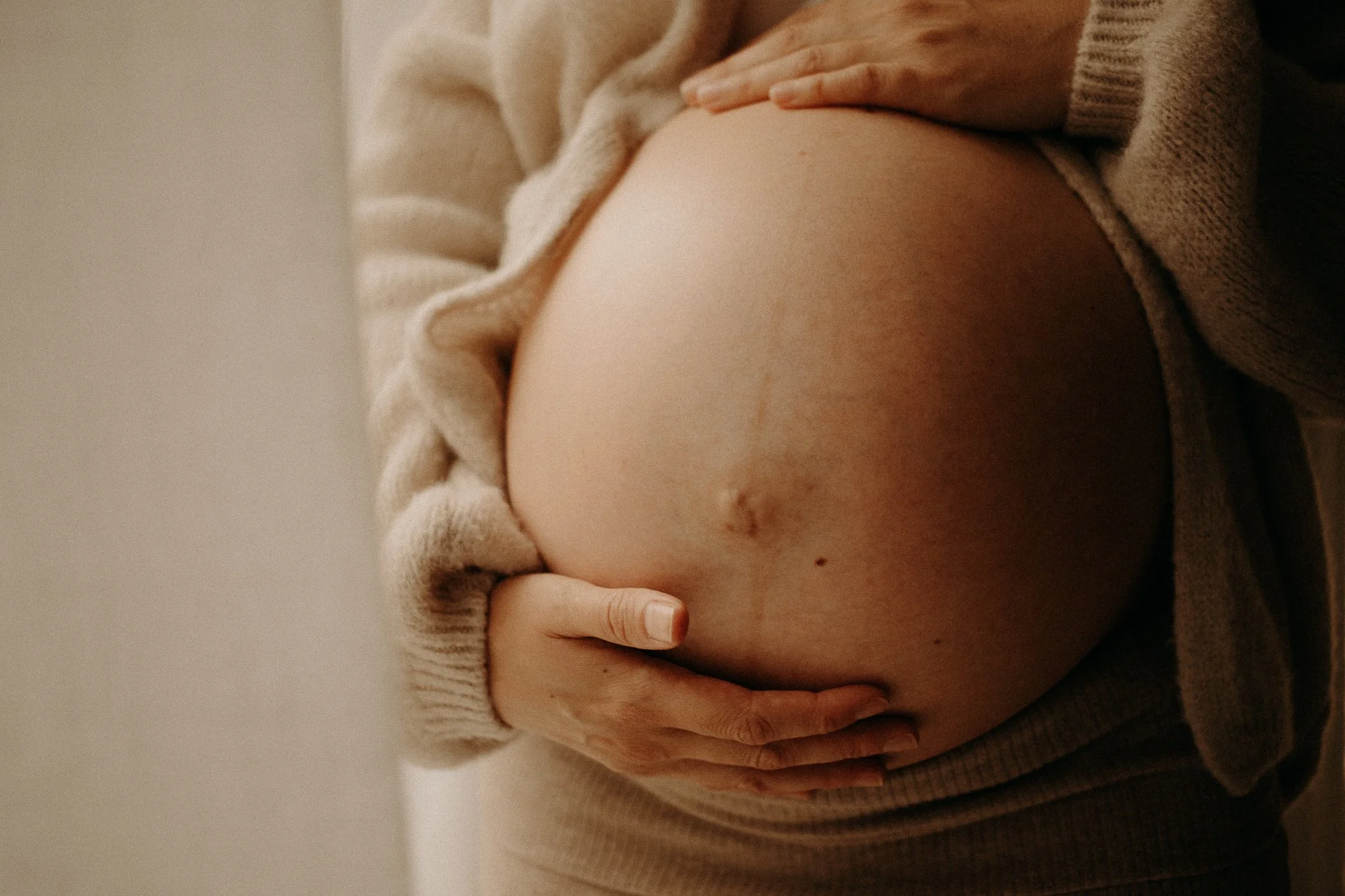 Une personne tenant son ventre rond, probablement une femme enceinte, portant un pull beige.