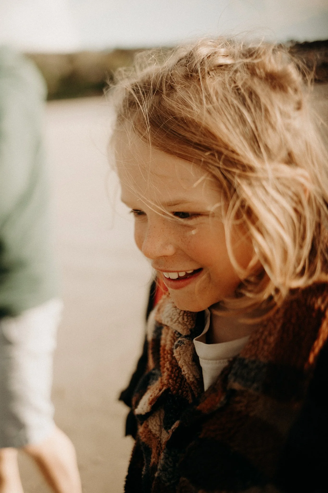 Jeune fille aux cheveux roux, souriante, portant une veste à carreaux, en plein air.