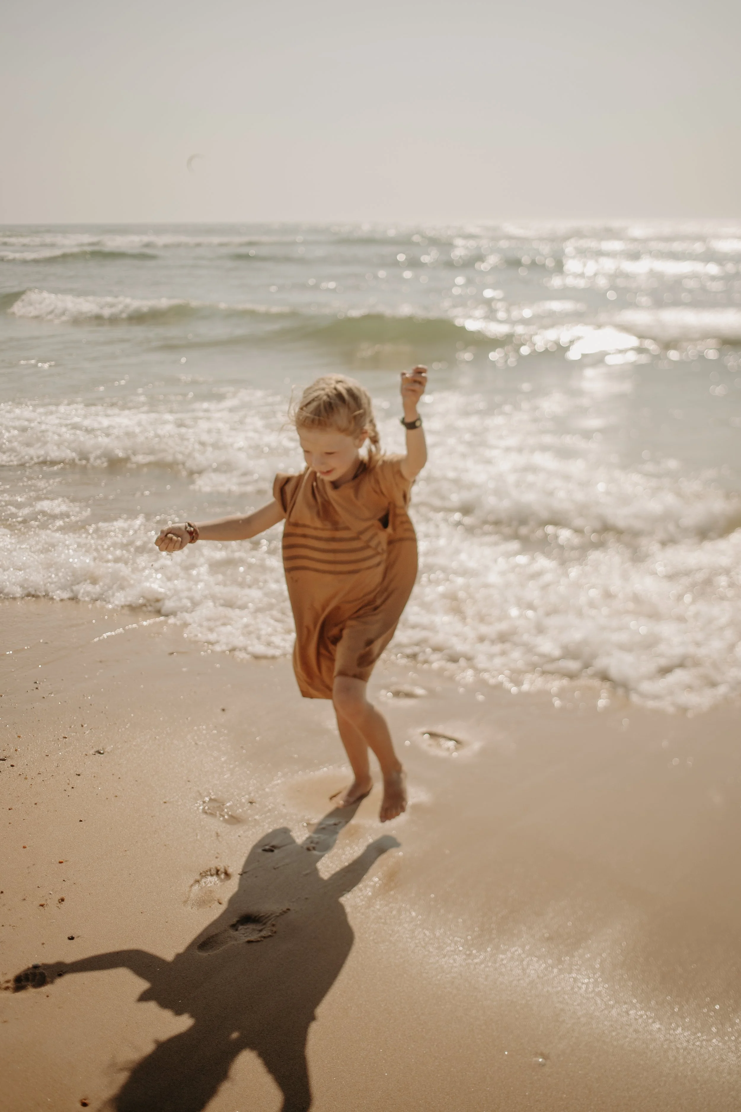 Un enfant souriant qui joue dans l'eau à la plage, avec des vagues et un ciel clair en arrière-plan.