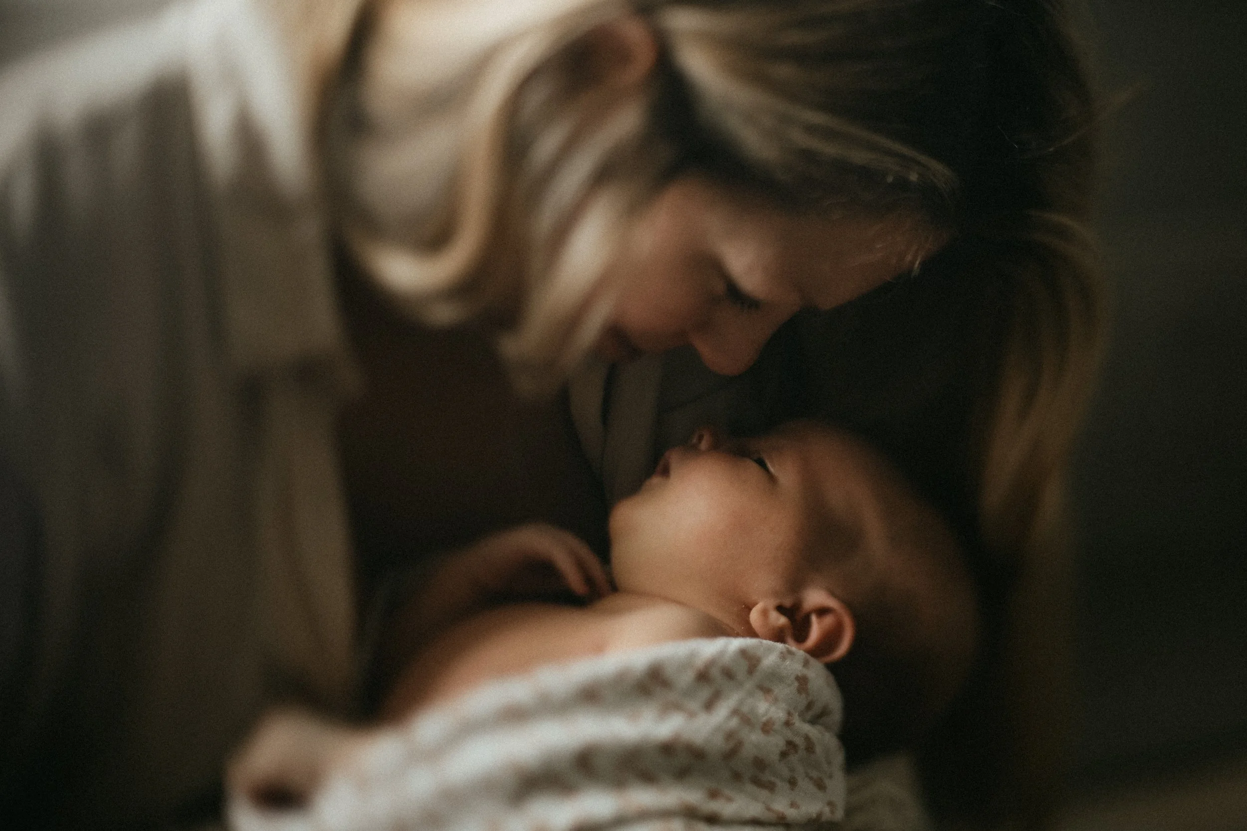 Une femme et un bébé se regardent tendrement, le visage de la femme au-dessus du bébé dans une lumière douce.