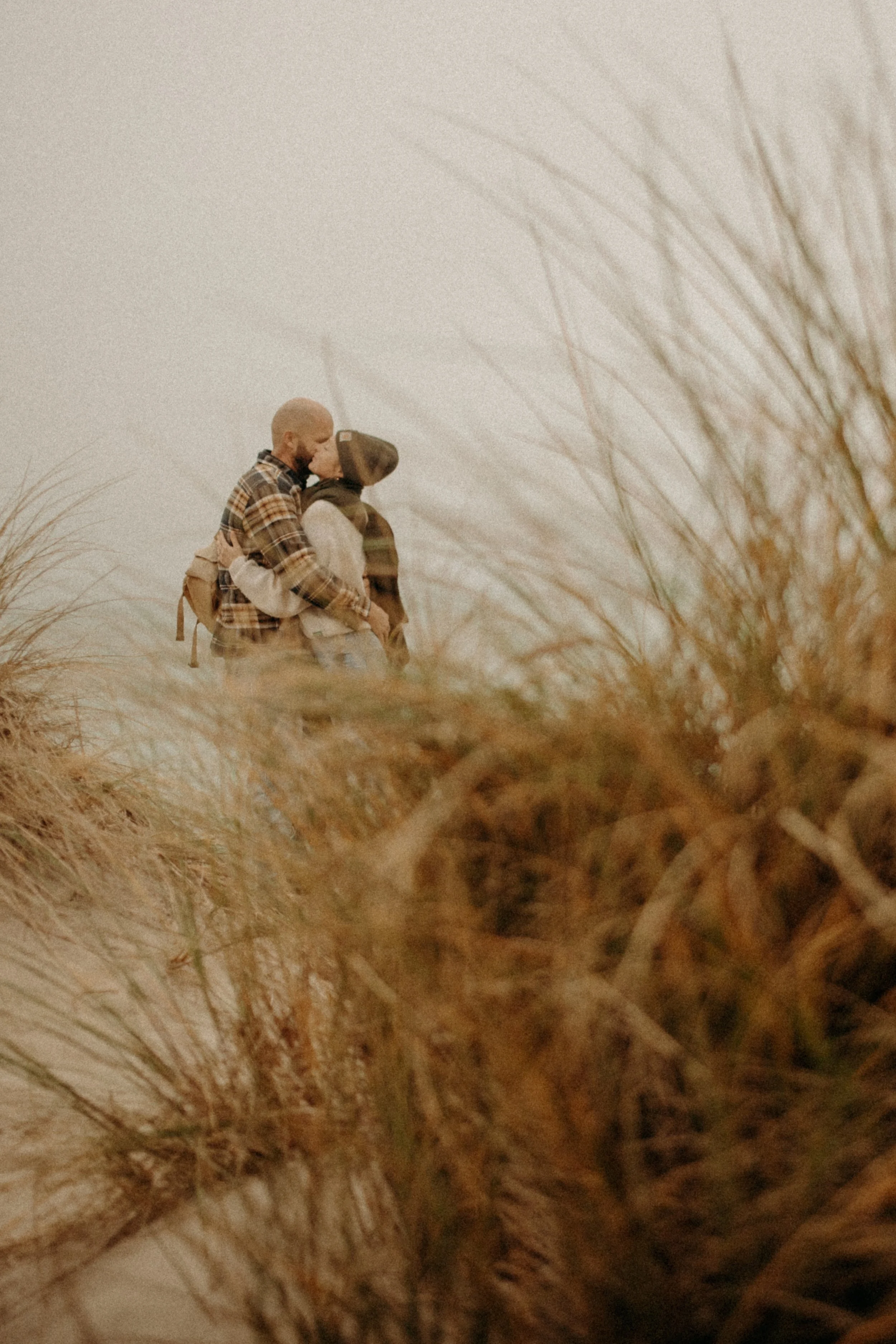 Deux personnes s'embrassent dans un champ de hautes herbes sèches, portant des vêtements d'automne.