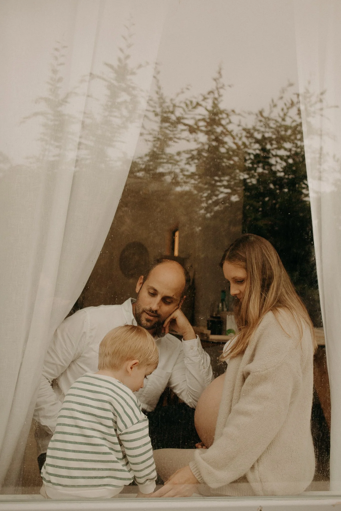 Photo d'une famille regardant par une fenêtre, avec une femme enceinte, un homme, un enfant, et deux parents.