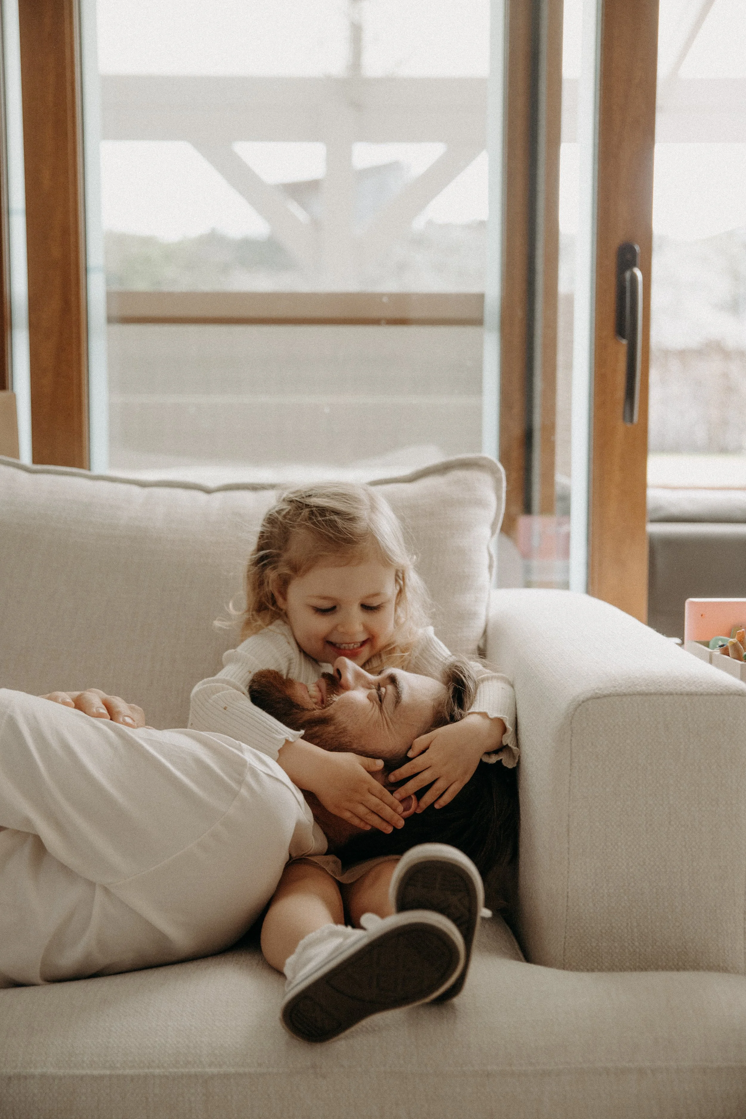 Une petite fille et un adulte jouent avec un chiot sur un canapé dans une maison.