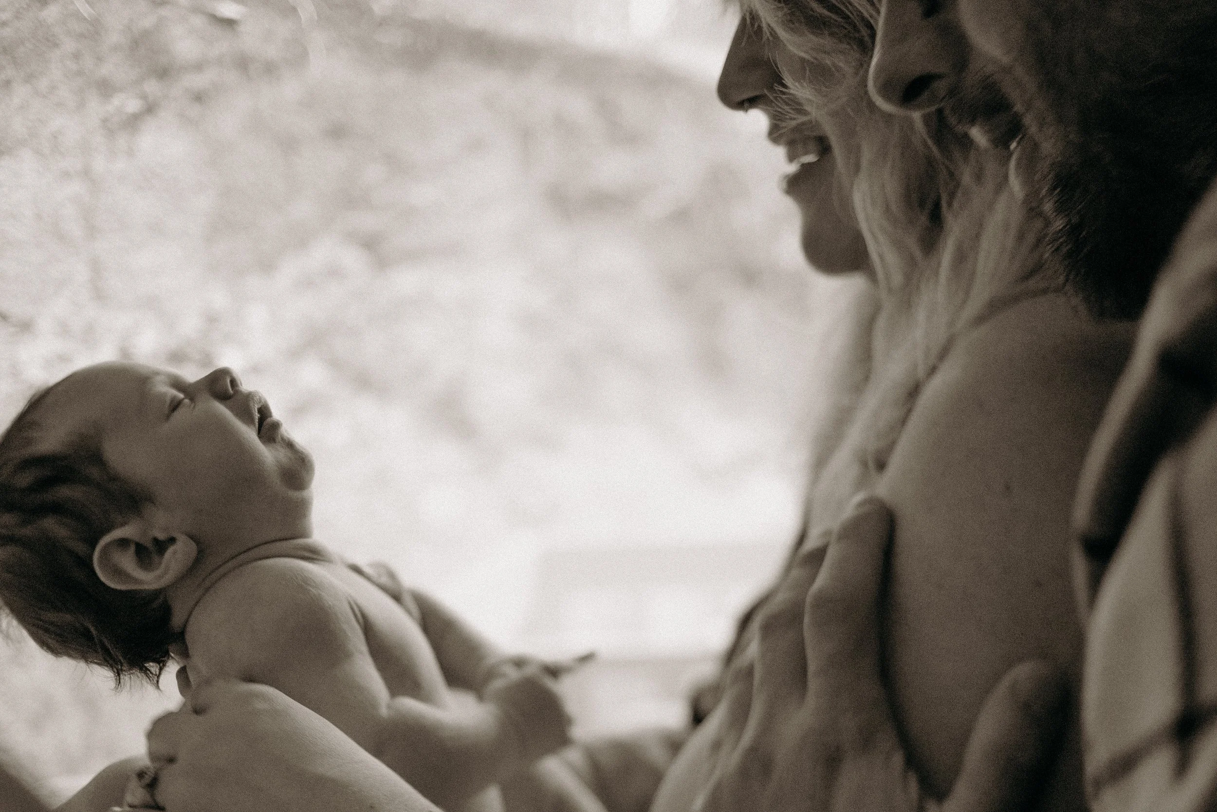 Une femme souriante tient un bébé dans ses bras, tous deux regardant l'un l'autre en étant proches.