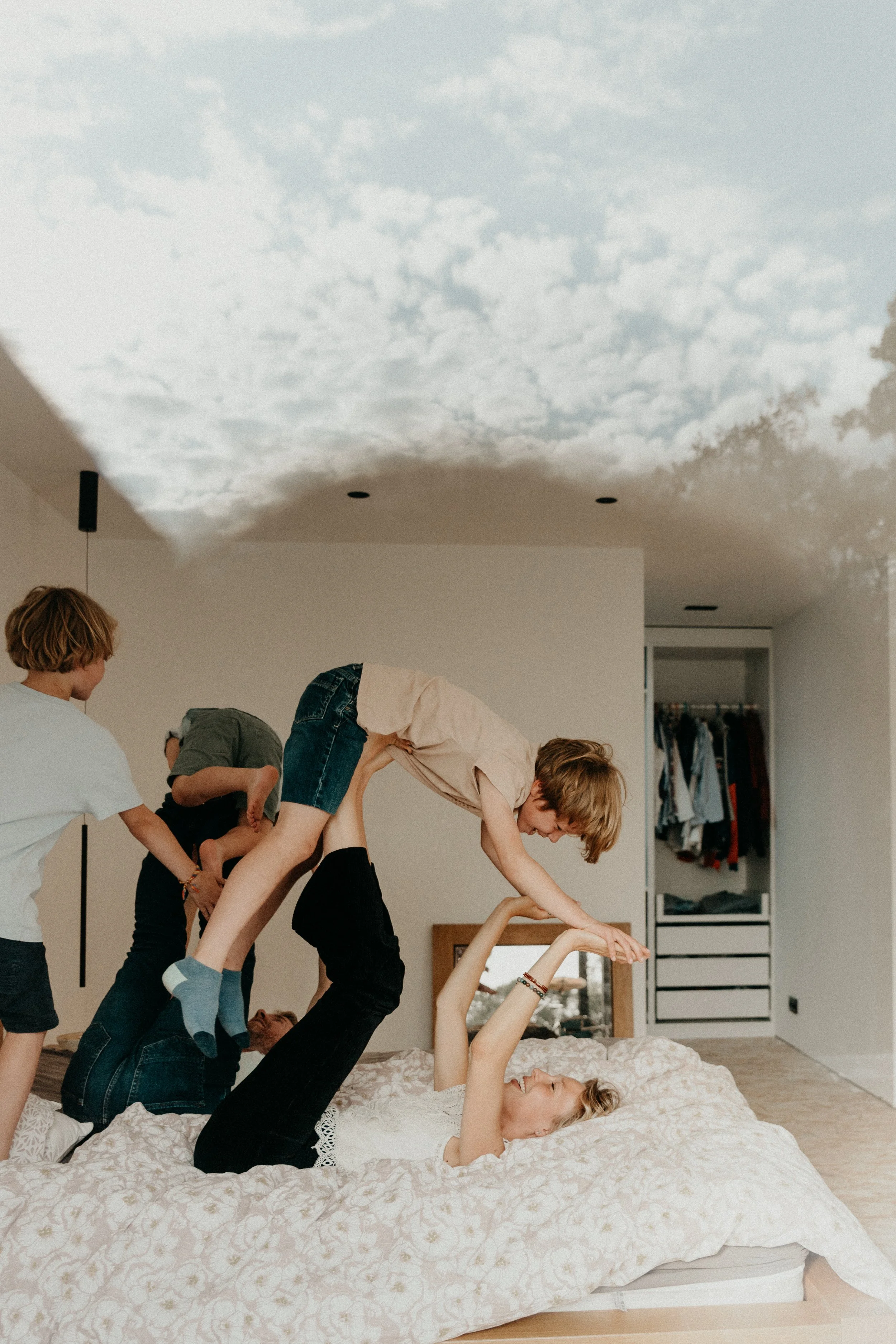 Une famille joue et s'amuse dans une chambre à coucher, formant une pyramide humaine sur un lit.