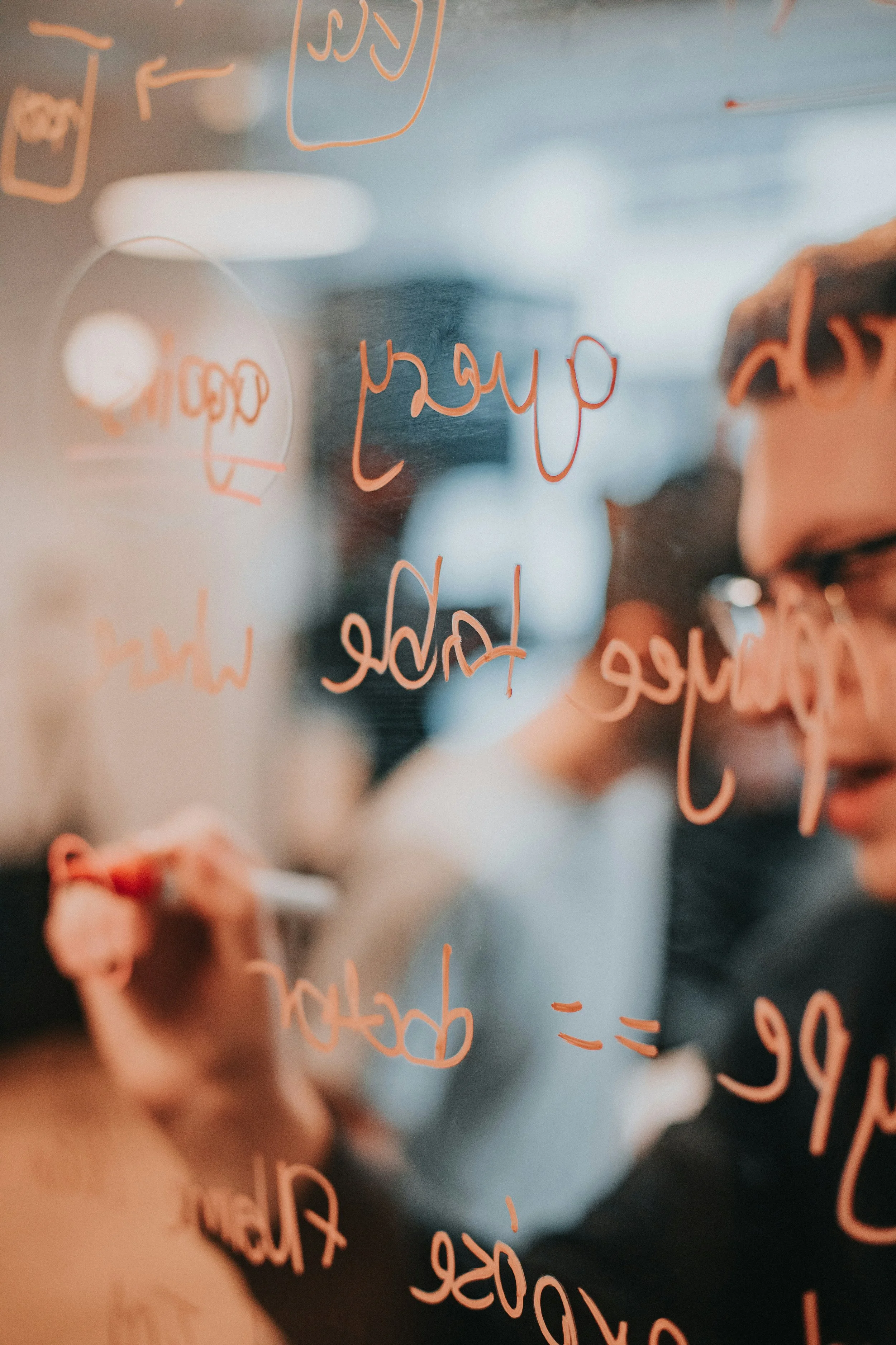 A person is writing on a transparent surface with a pink marker, creating a list or notes. The person is bending forward, focusing on their writing.